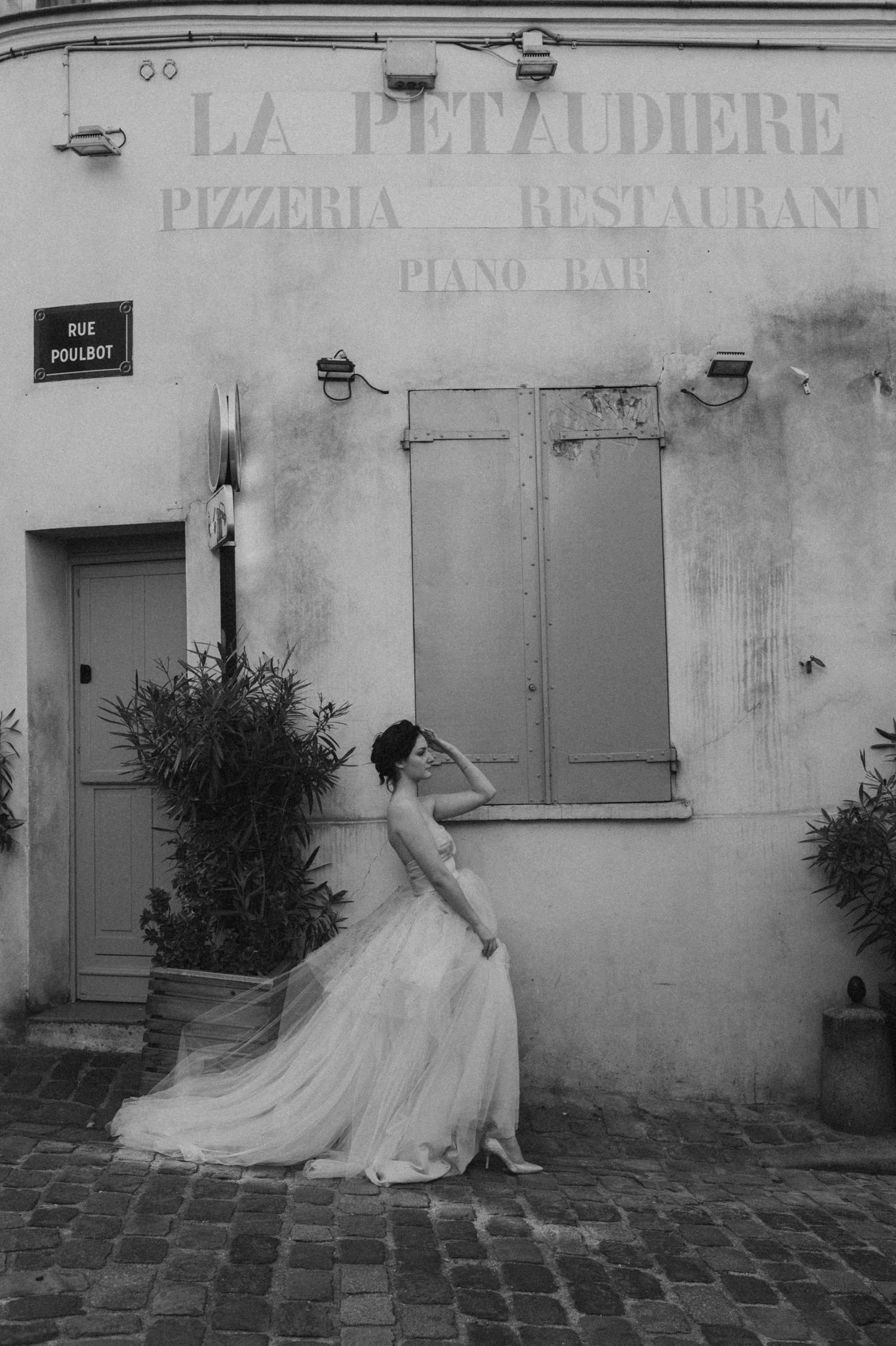 A romantic black and white bridal portrait against a rustic French restaurant facade with a blue door.