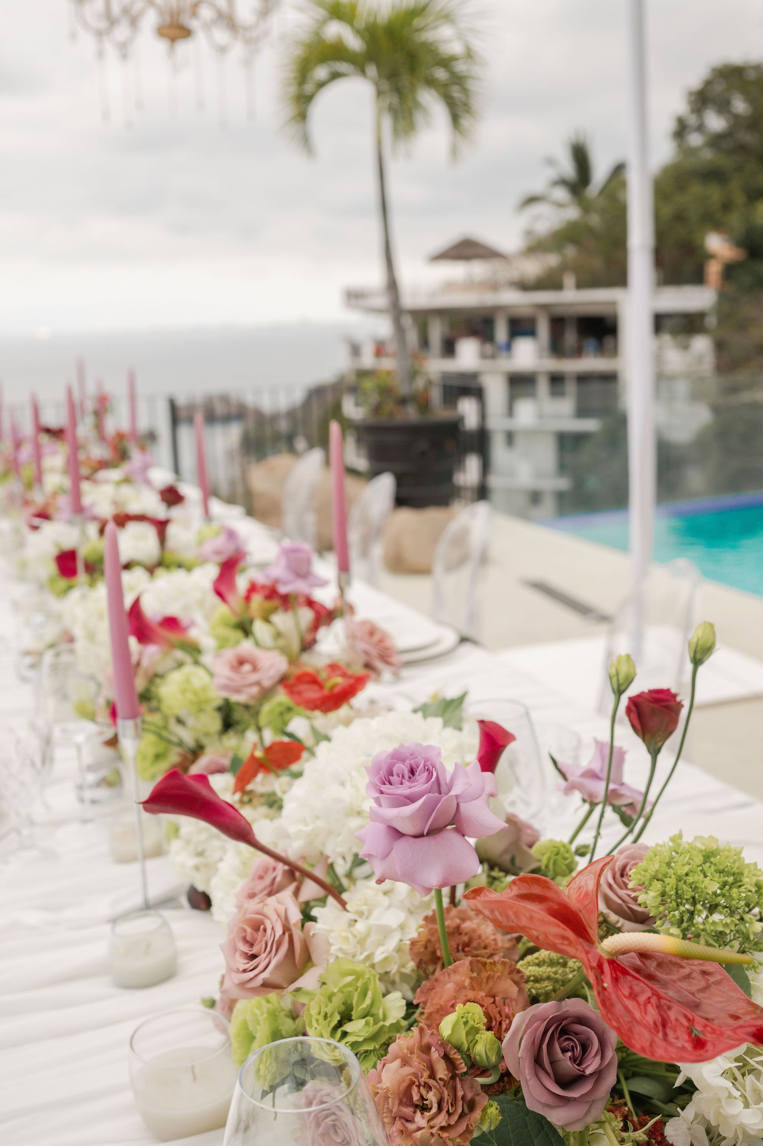 Elegant wedding reception table with lush floral centerpieces of pink roses, anthuriums, and greenery with pink taper candles.