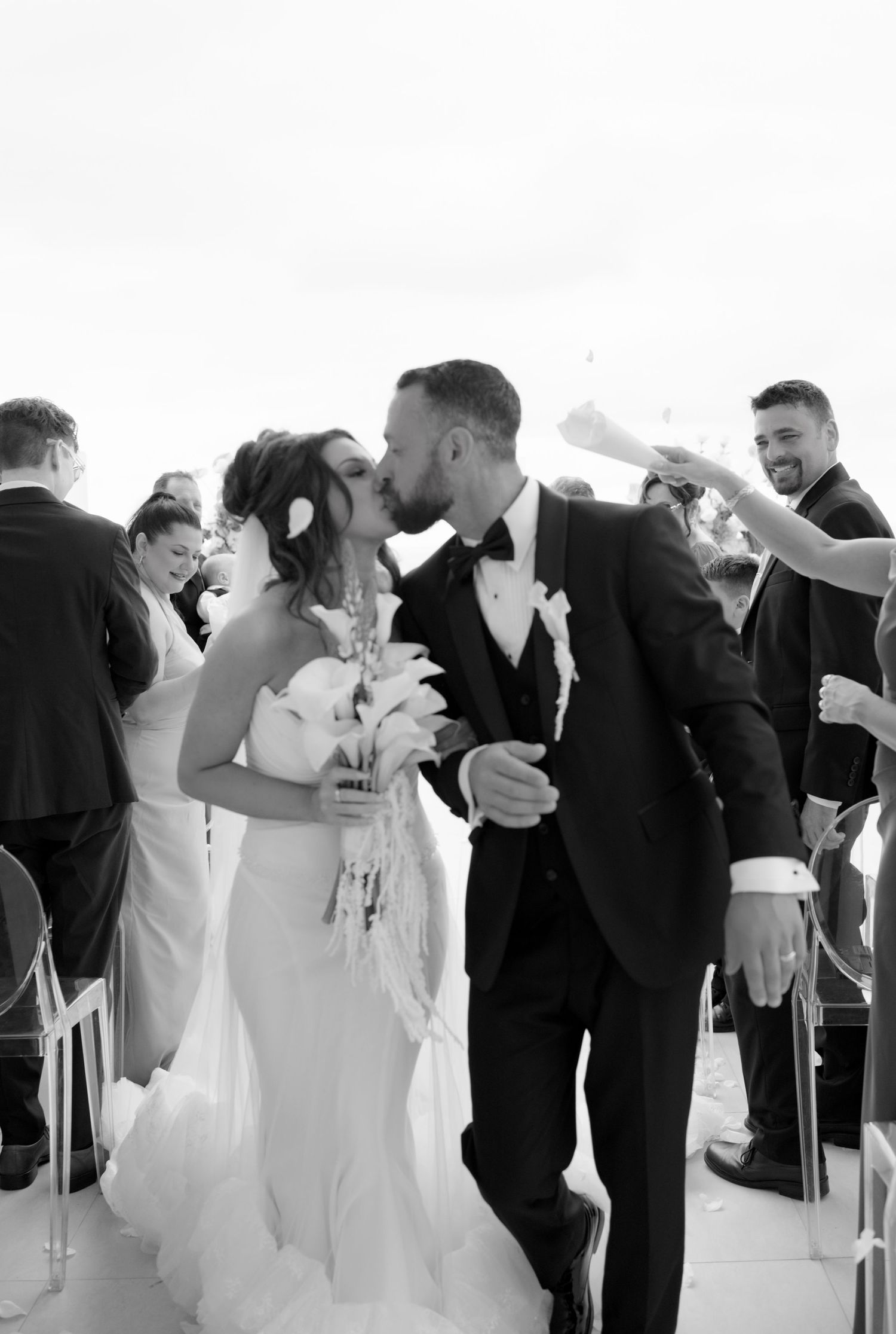 Black and white photo of a bride and groom sharing a kiss while walking down the aisle at their wedding ceremony.