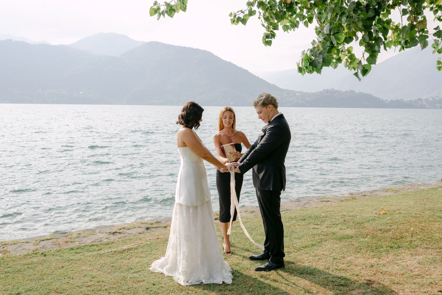 Couple exchanging vows in a lakeside wedding ceremony with mountain backdrop and officiant.
