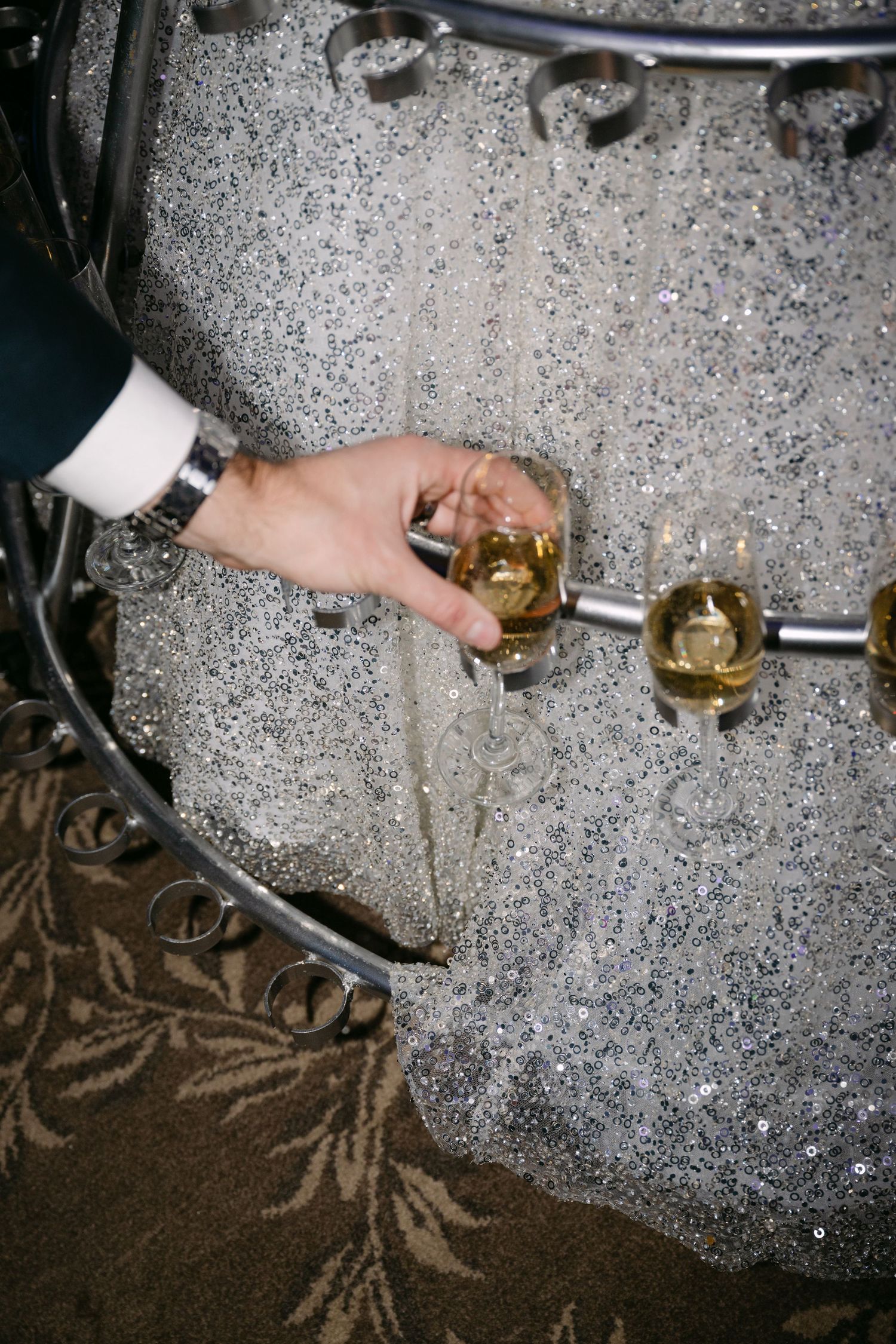 Guest taking a champagne glass from a performer's elaborate silver hoop skirt dress at a formal event.
