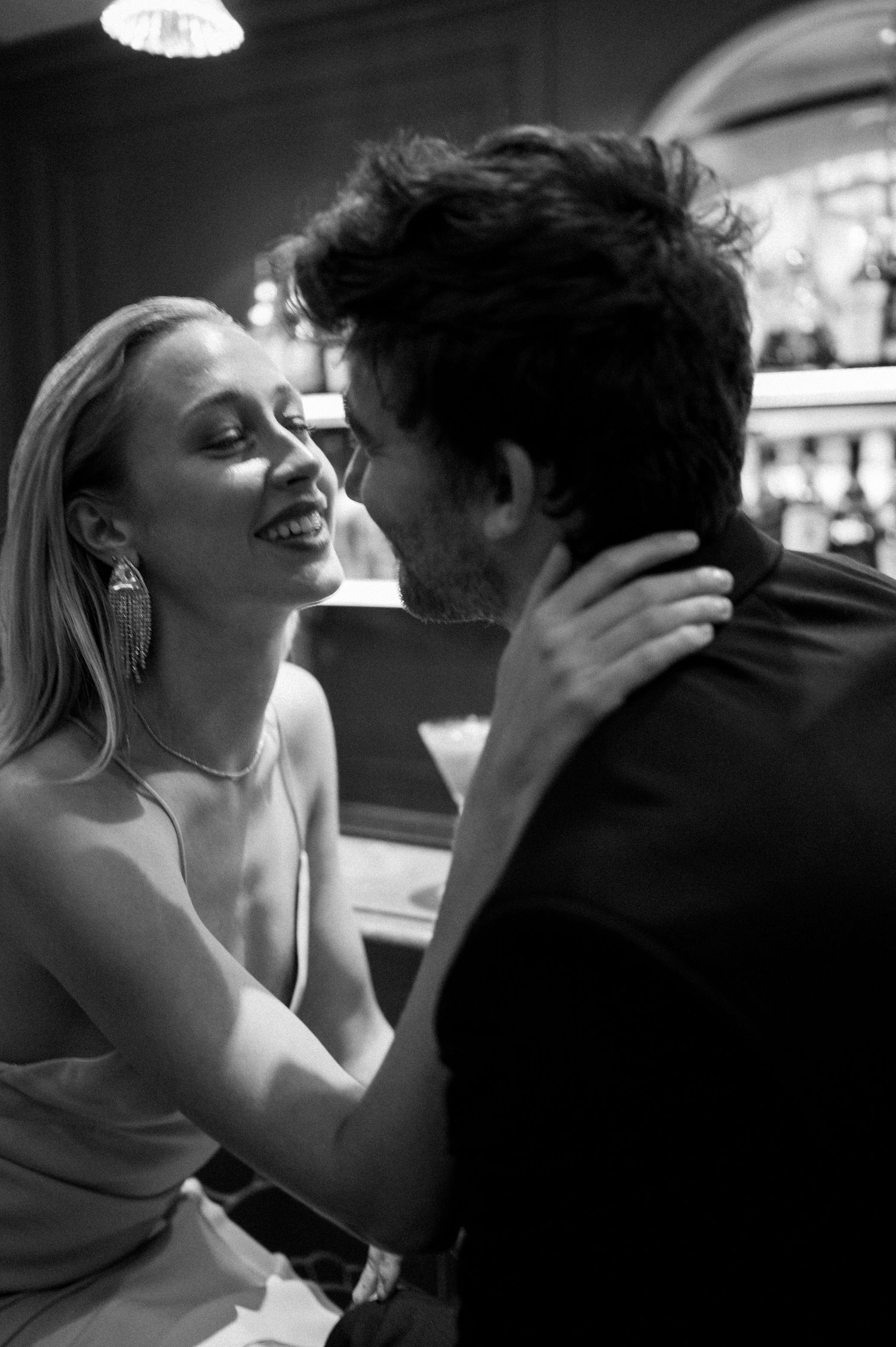 Black and white photo of smiling woman embracing man at a bar, radiating joy and romance.