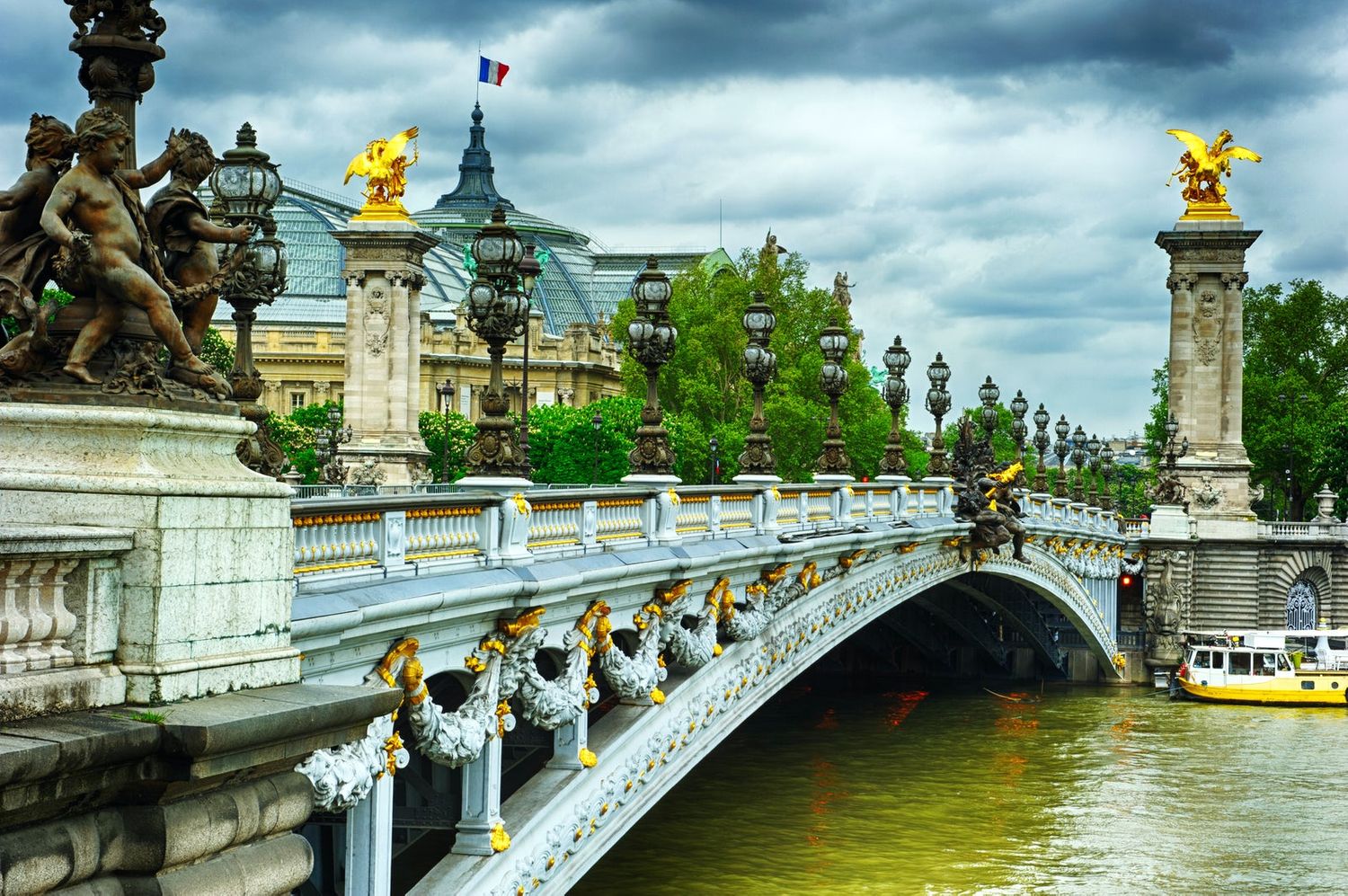 Pont Alexandre III bridge in Paris with ornate golden statues and dramatic stormy sky.