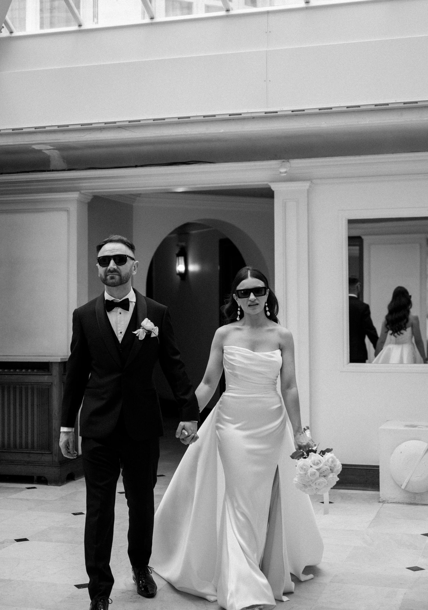 Stylish bride and groom in sunglasses walking together in modern black and white photography.
