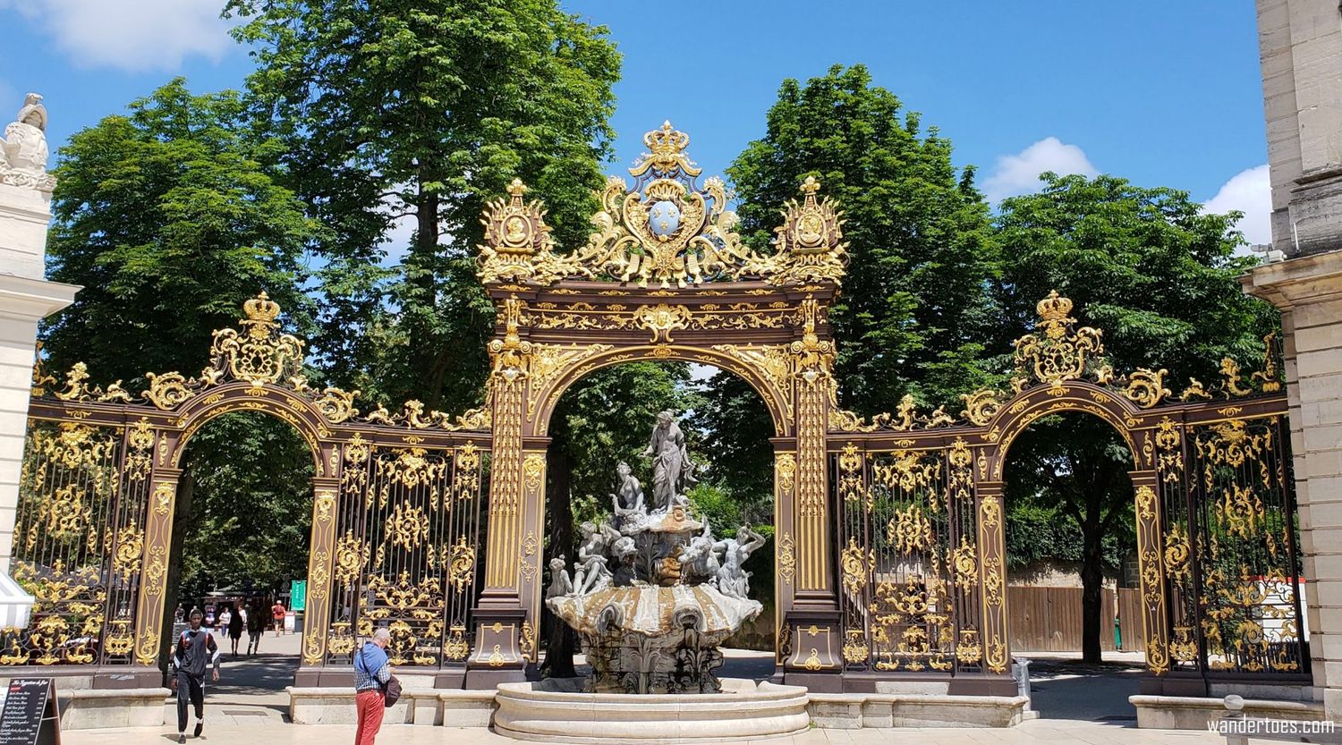 Ornate golden gates with decorative metalwork at the entrance to a European palace or park.