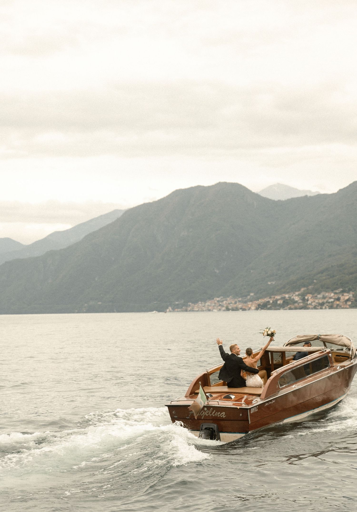 Wooden vintage boat cruising on lake with mountains in background.