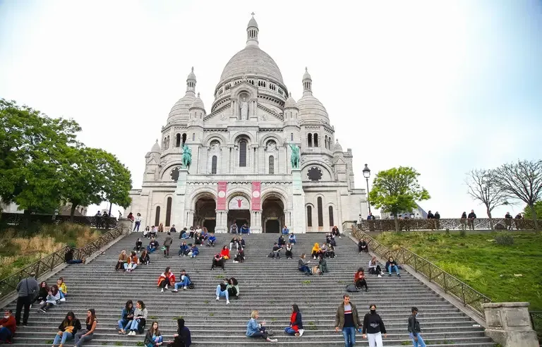 Sacre Coeur basilica in Paris with tourists sitting on the famous steps.
