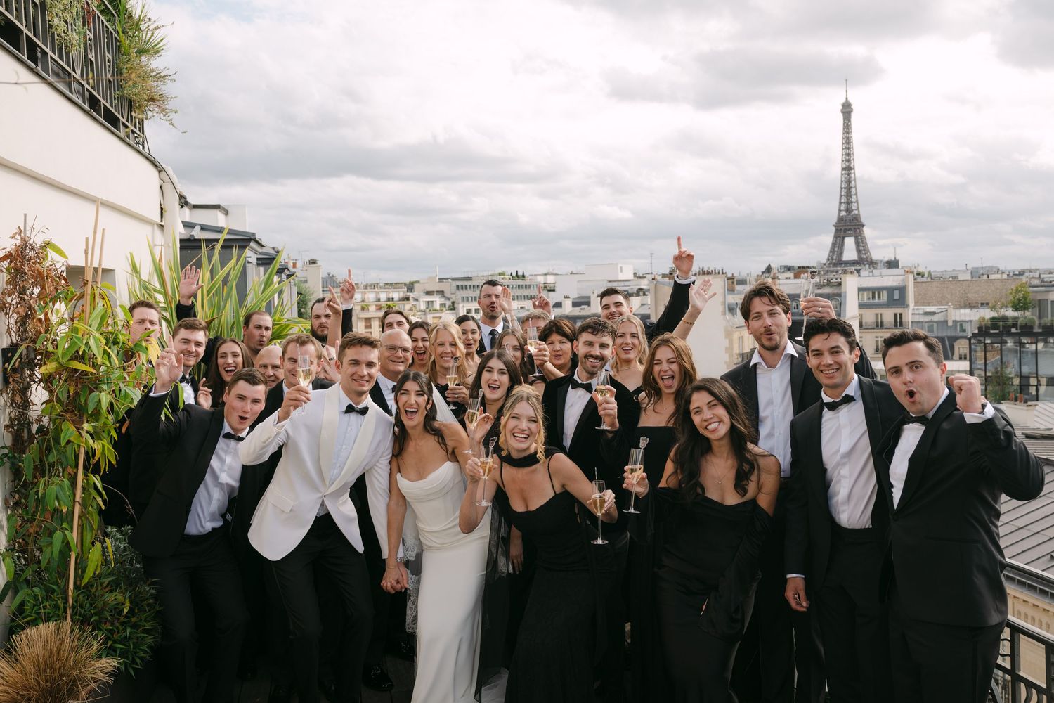 Wedding party group photo on a Paris rooftop terrace with the Eiffel Tower in the background.