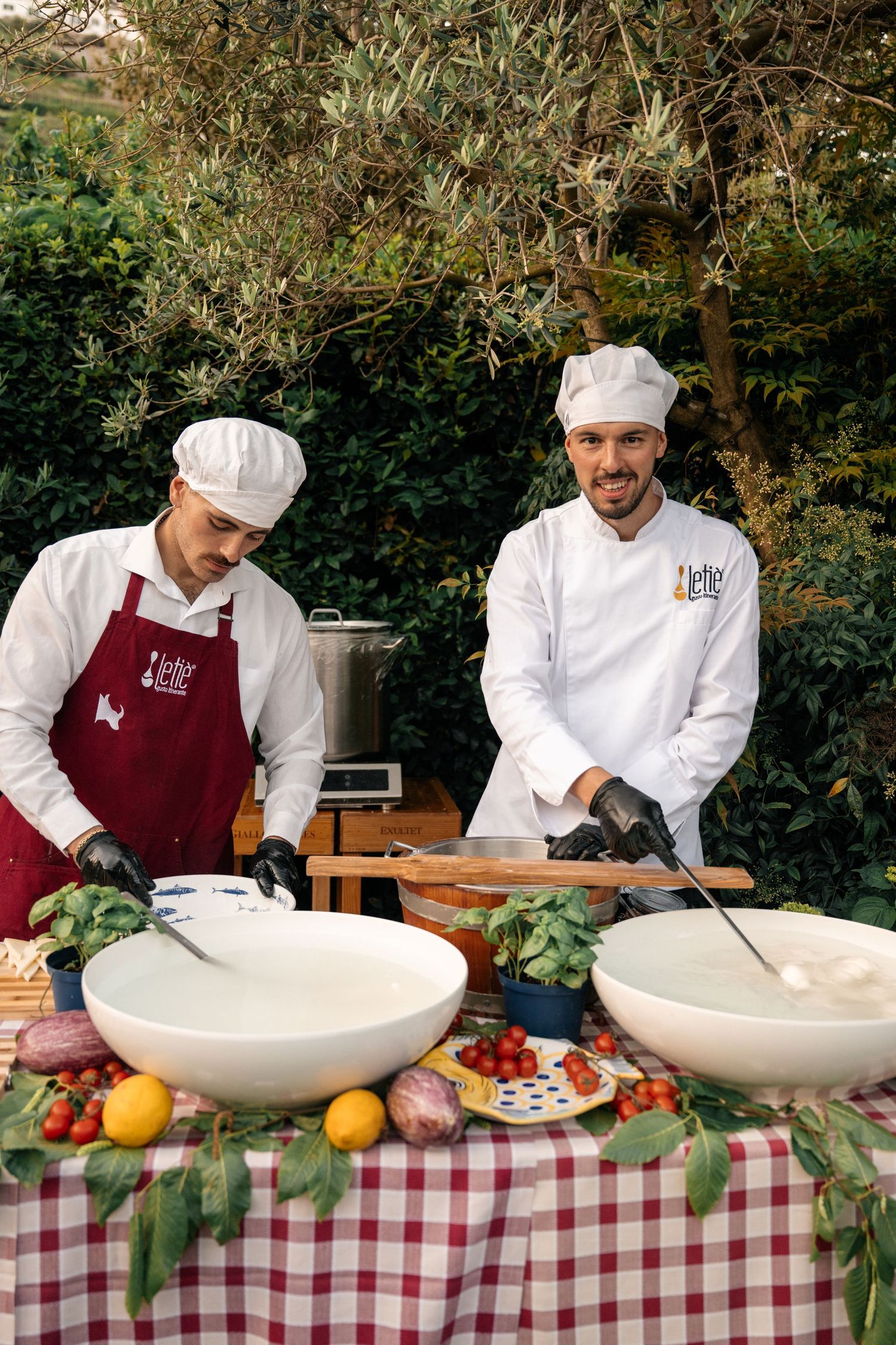 Two chefs in white uniforms preparing fresh mozzarella outdoors at Italian wedding catering station.