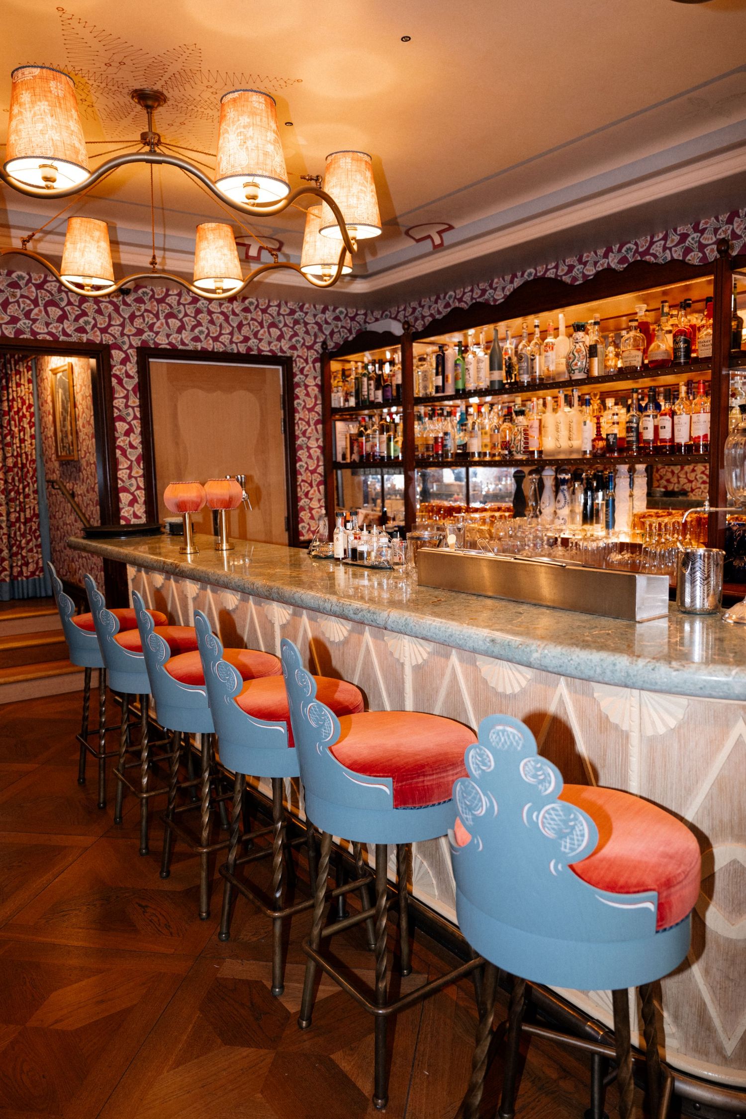Elegant bar interior featuring blue and orange bar stools, chandelier lighting, and stocked shelves.