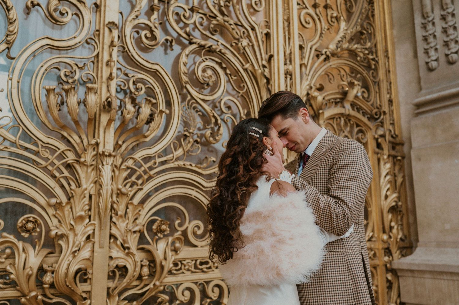 Romantic wedding moment captured against intricate golden architectural backdrop.