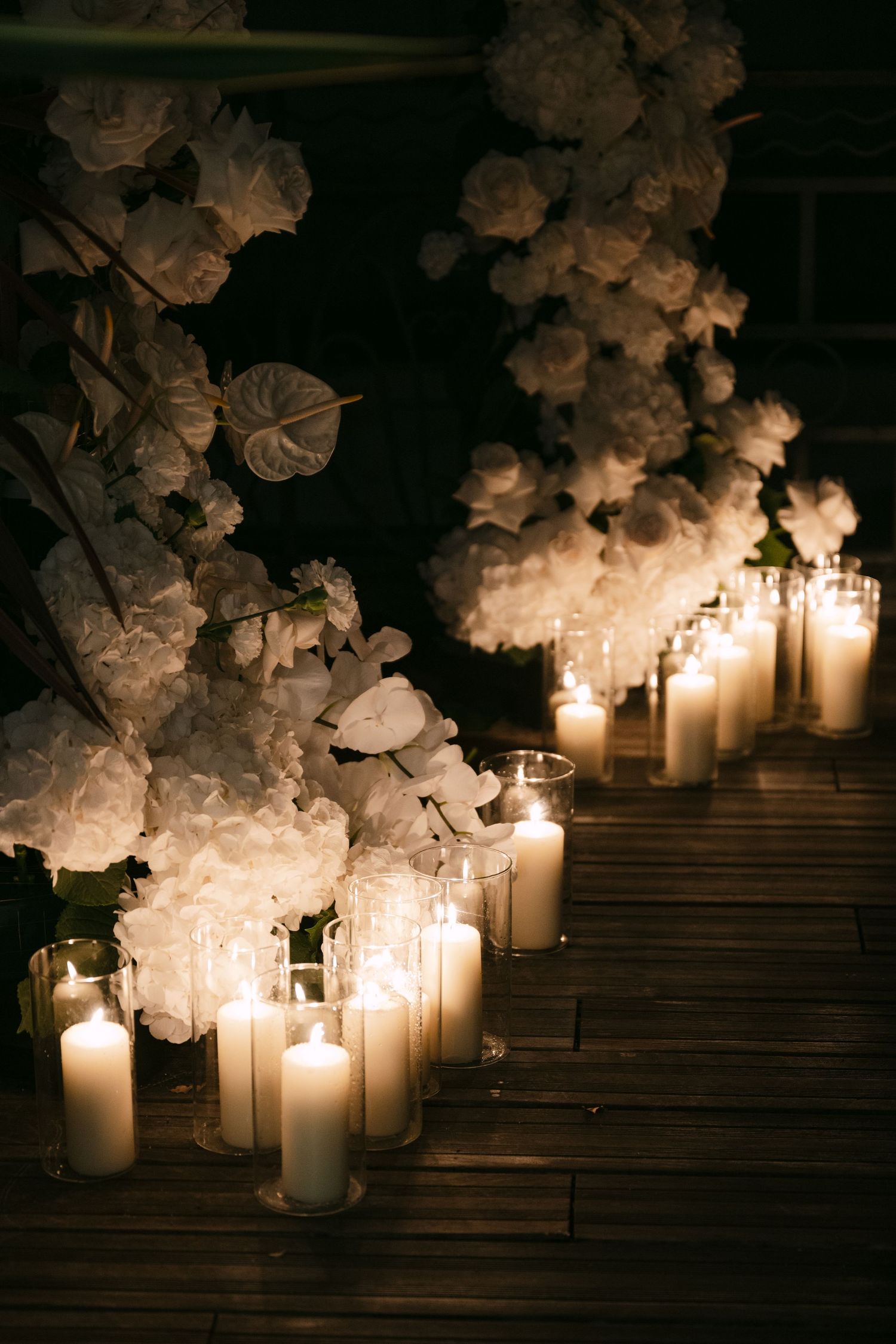 White orchids and glowing candles create a romantic ambiance on dark wooden steps in a dimly lit setting.