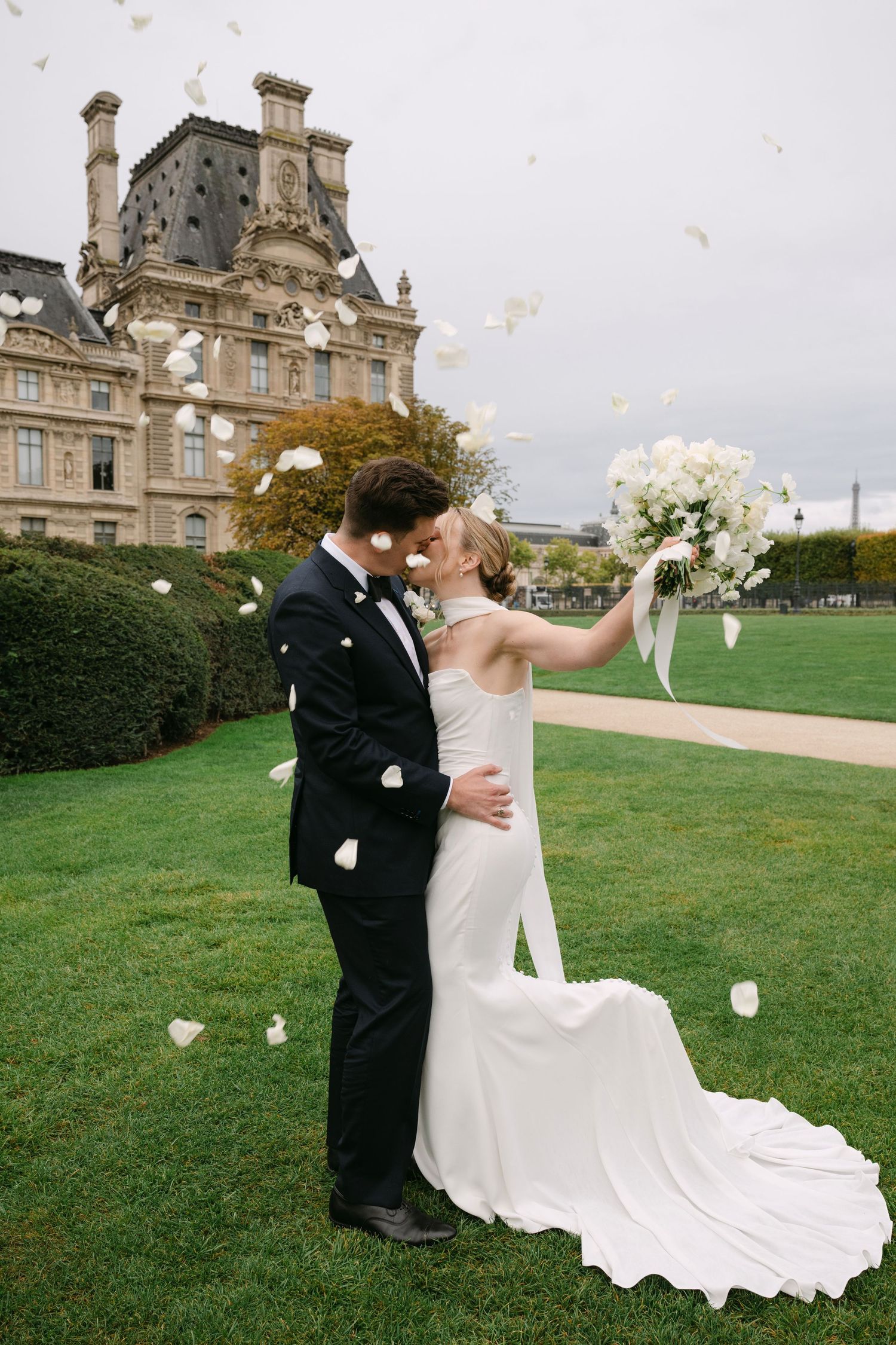 A couple in wedding attire shares a romantic moment on a manicured lawn with a grand chateau in the background.