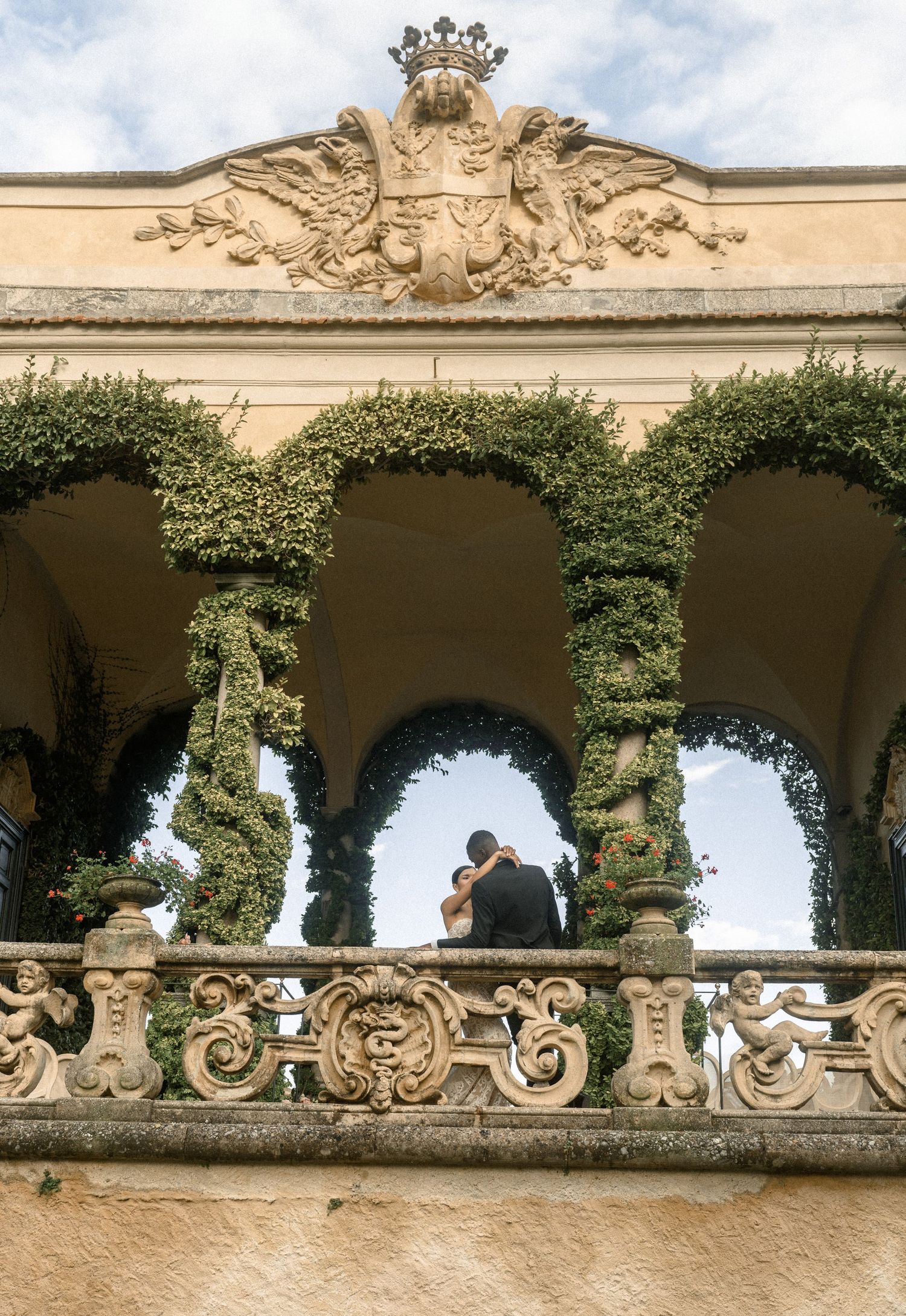 Couple embracing under ornate stone arches with climbing ivy and carved architectural details.