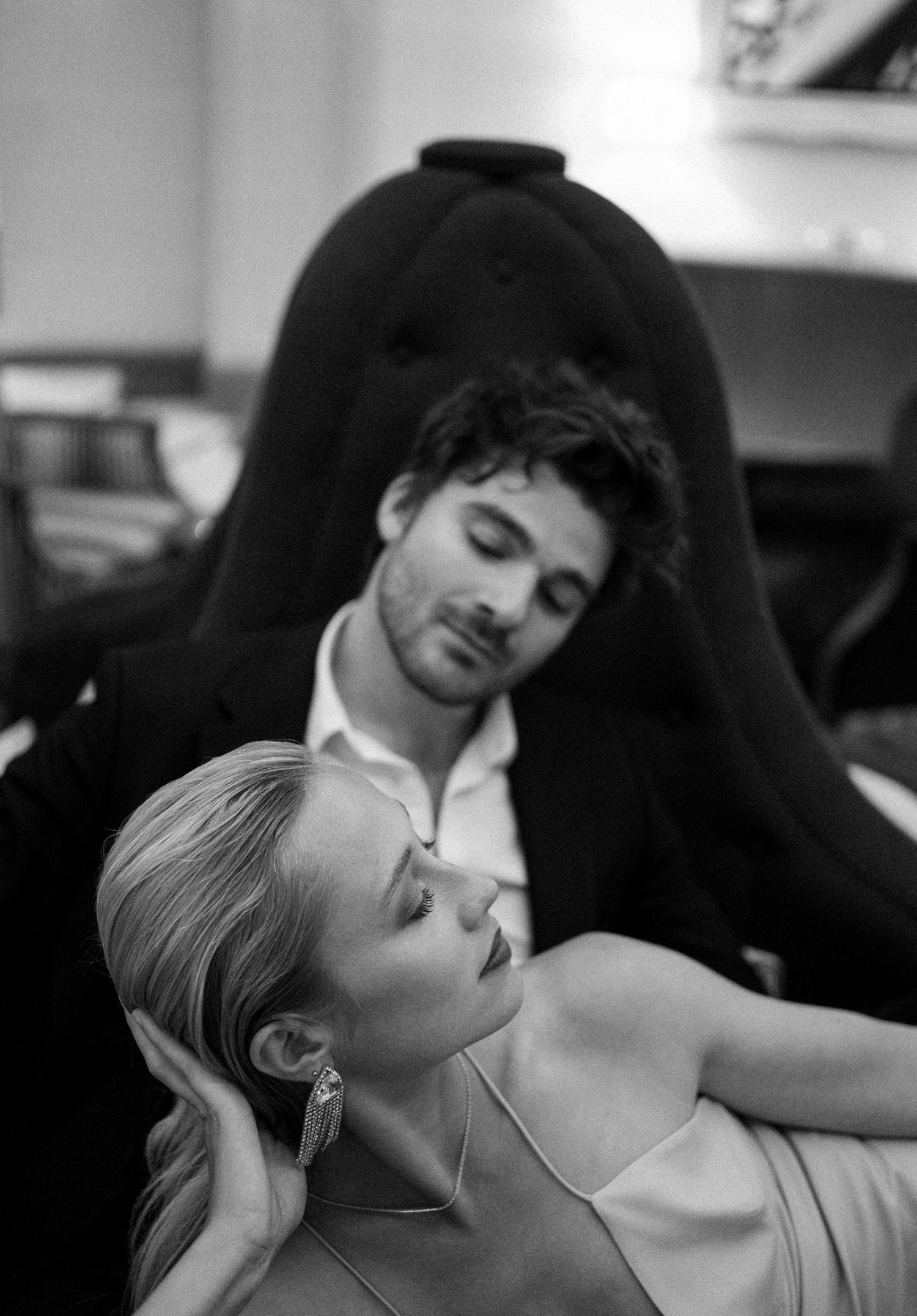Black and white intimate portrait of a couple resting together on a tufted velvet chair.