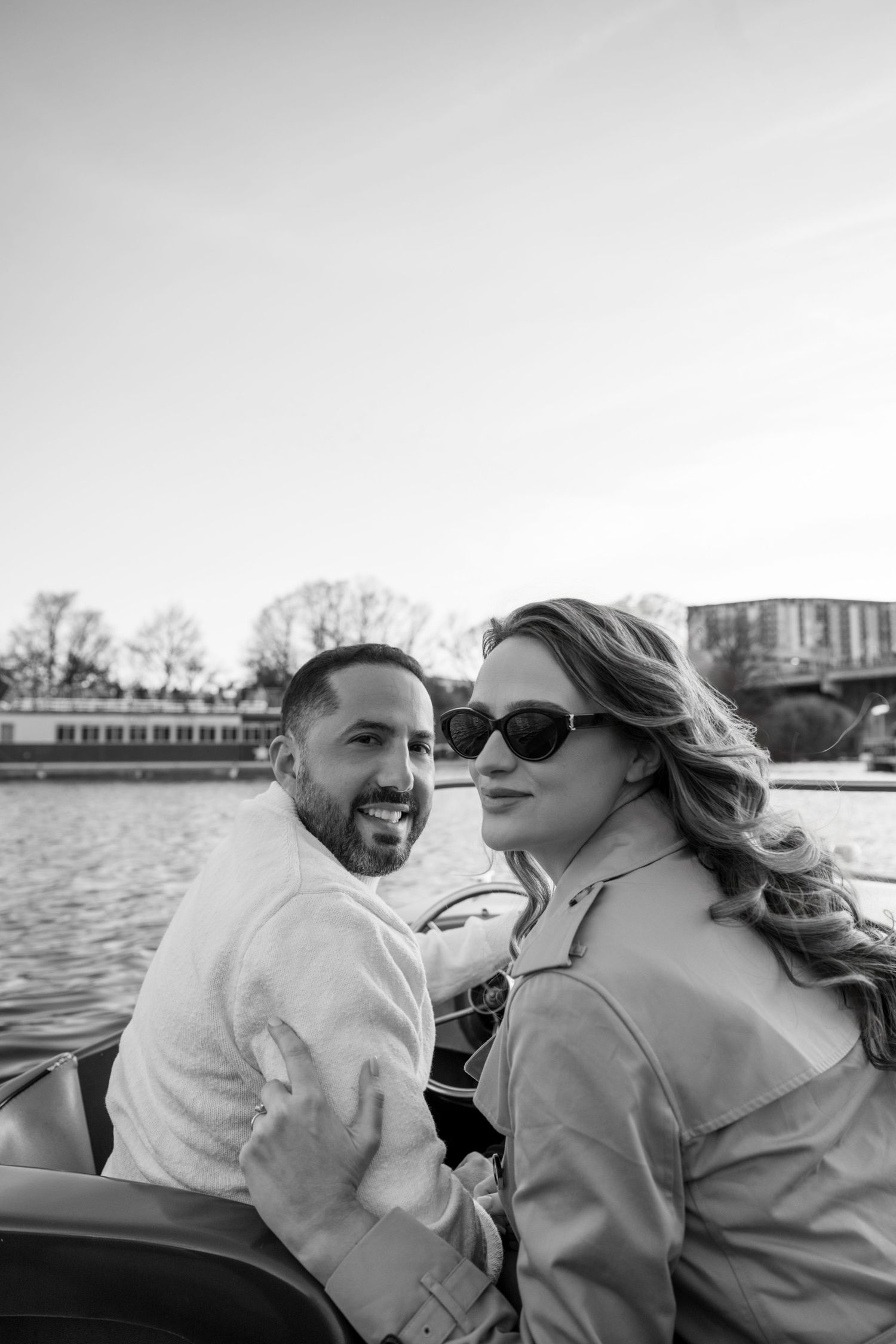 Black and white photo of a smiling couple on a boat near a bridge.