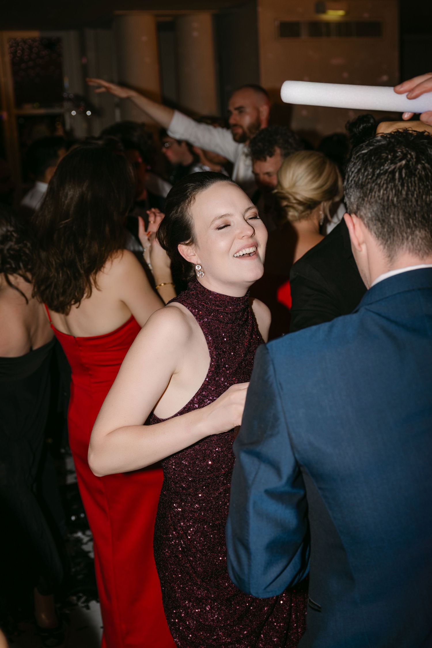Woman in burgundy sequin halter dress laughing and dancing at a formal wedding reception party.