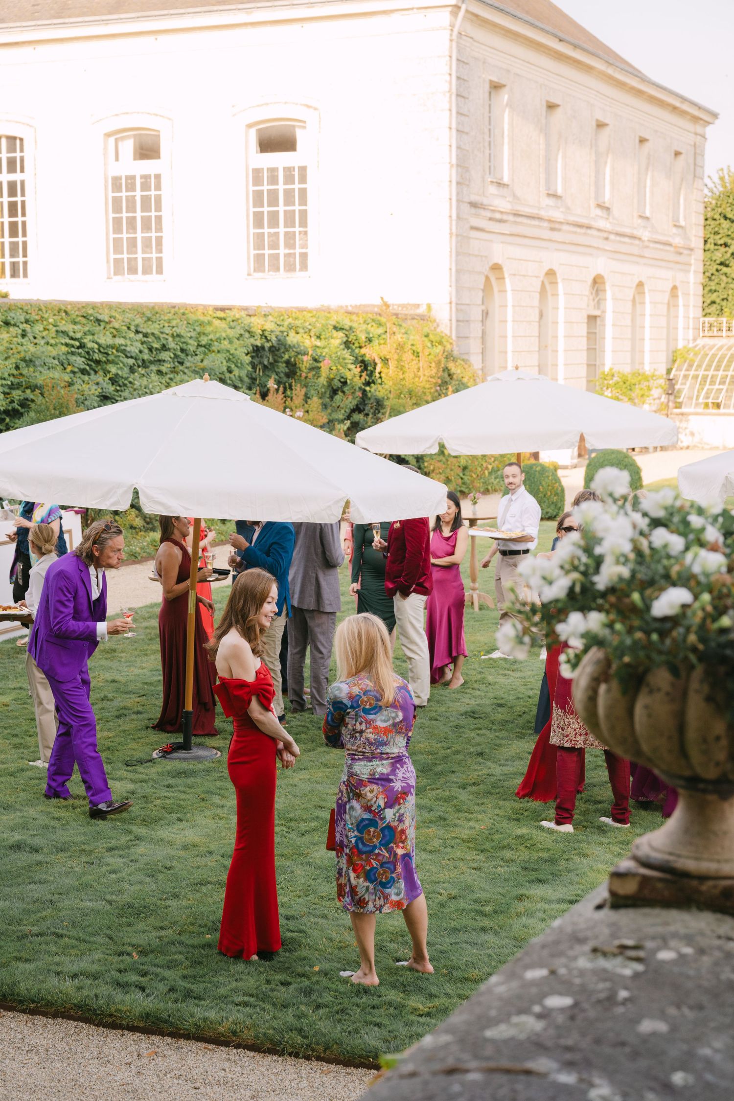 Wedding guests mingling on manicured lawn under white canopy tents at French chateau celebration.