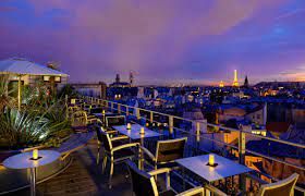 Illuminated rooftop terrace with blue lighting and Paris skyline views at dusk.