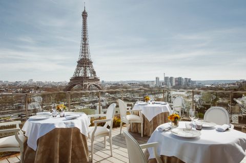 Elegant rooftop dining tables with white tablecloths overlooking the Eiffel Tower in Paris.