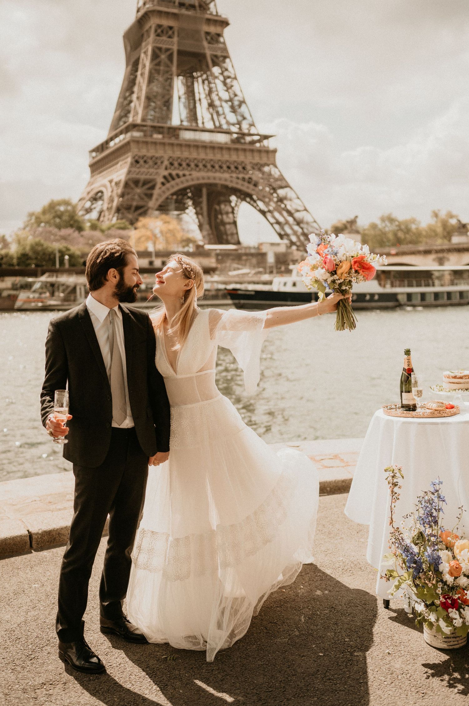 Bride in flowing dress celebrates with groom during Paris wedding photoshoot.