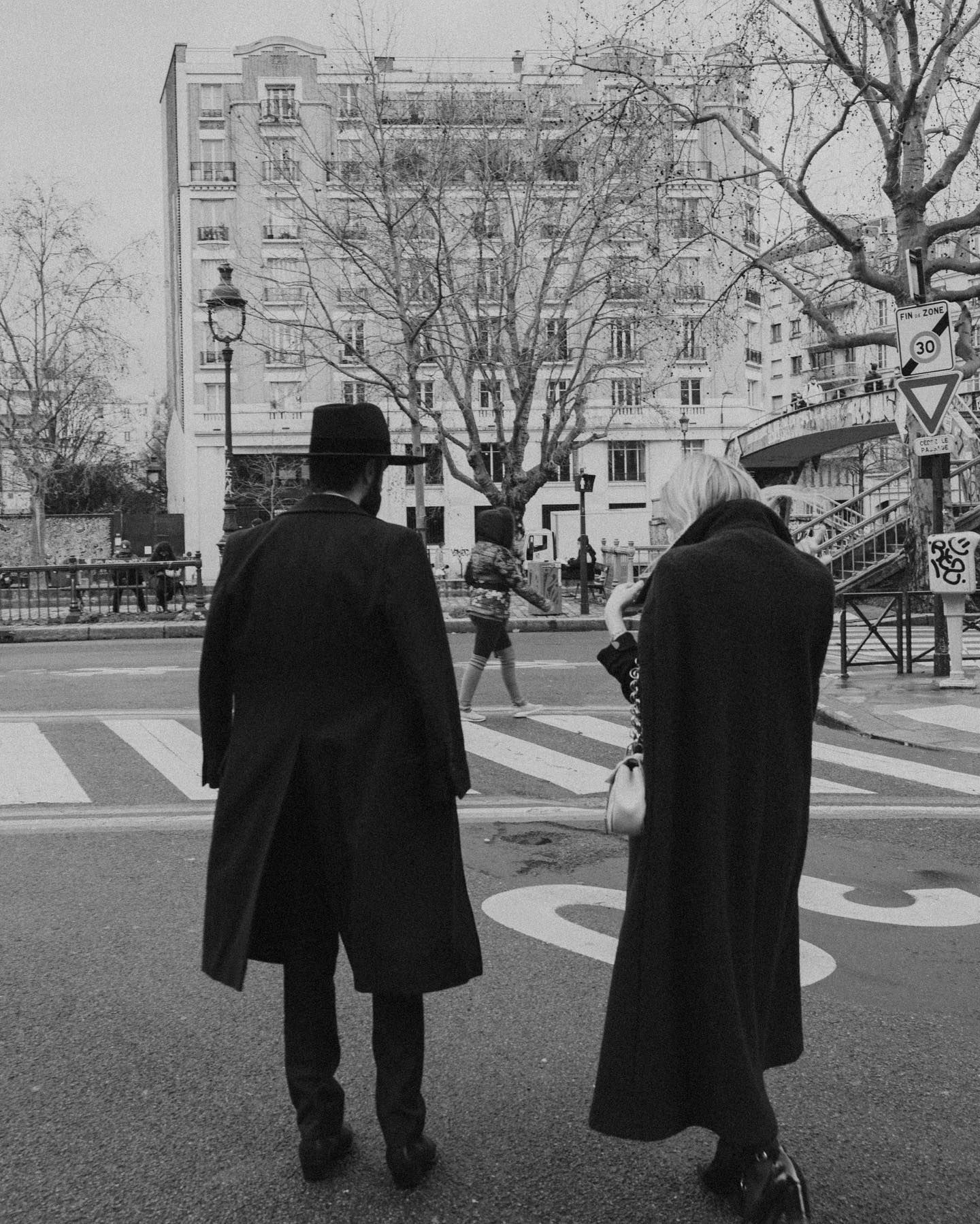 Two figures in long coats walking along a Parisian street in winter.