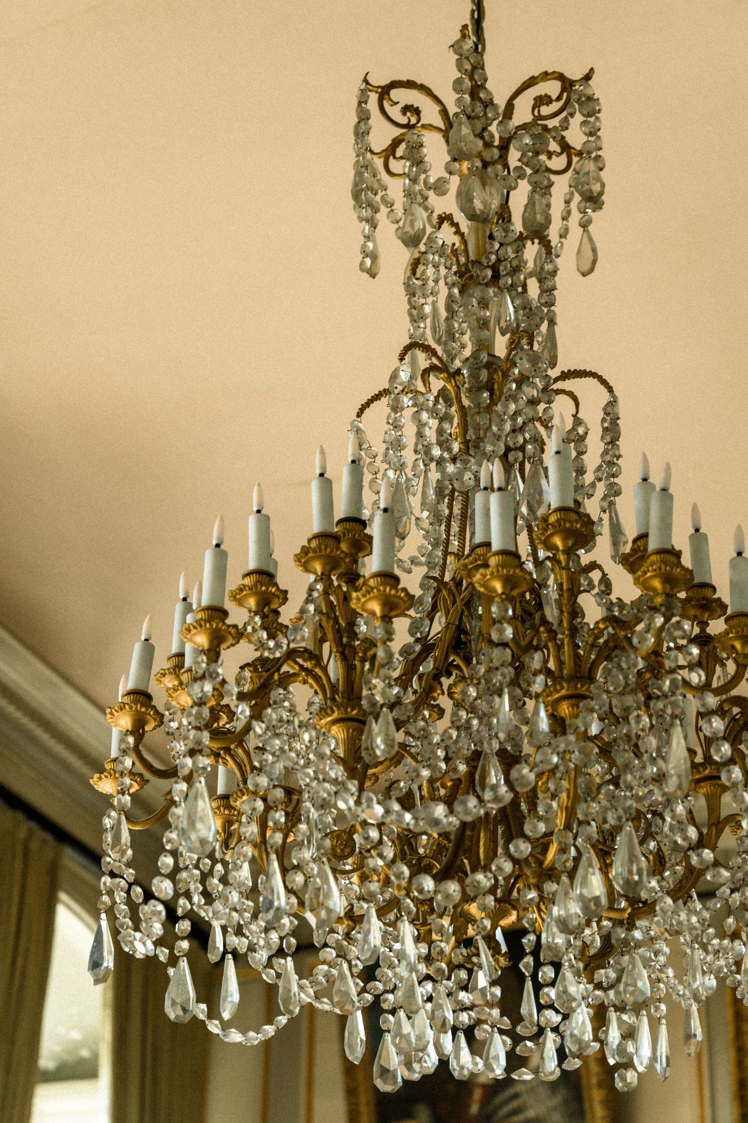 Ornate crystal and gold chandelier with multiple tiers hangs in an elegant room.