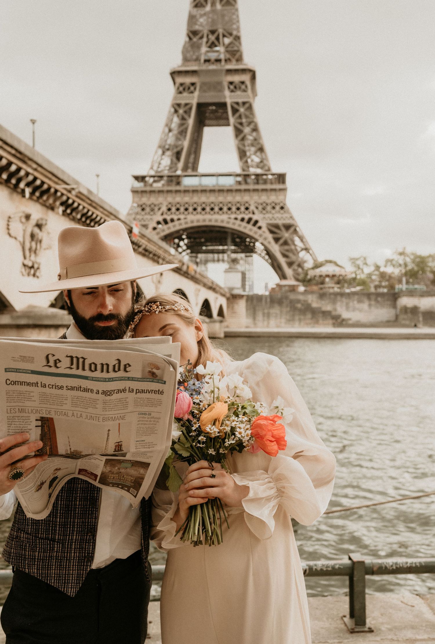 A sepia-toned photograph of a couple sharing a moment with newspaper and flowers by the Eiffel Tower.