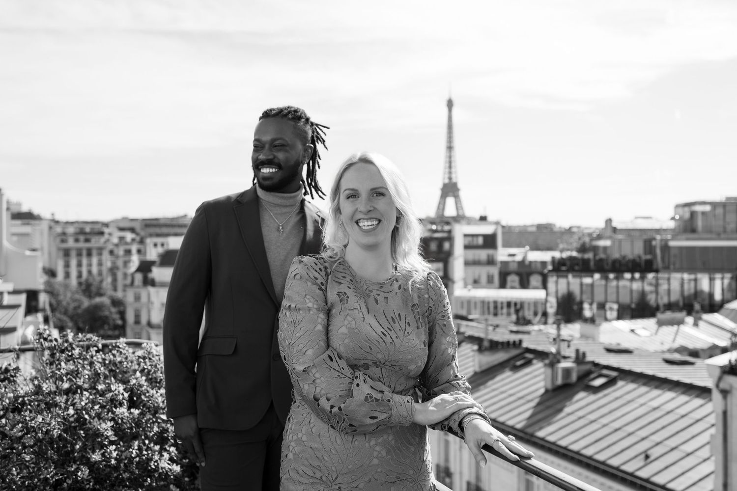 Couple smiling on a rooftop in Paris with the Eiffel Tower in the background, black and white photo.