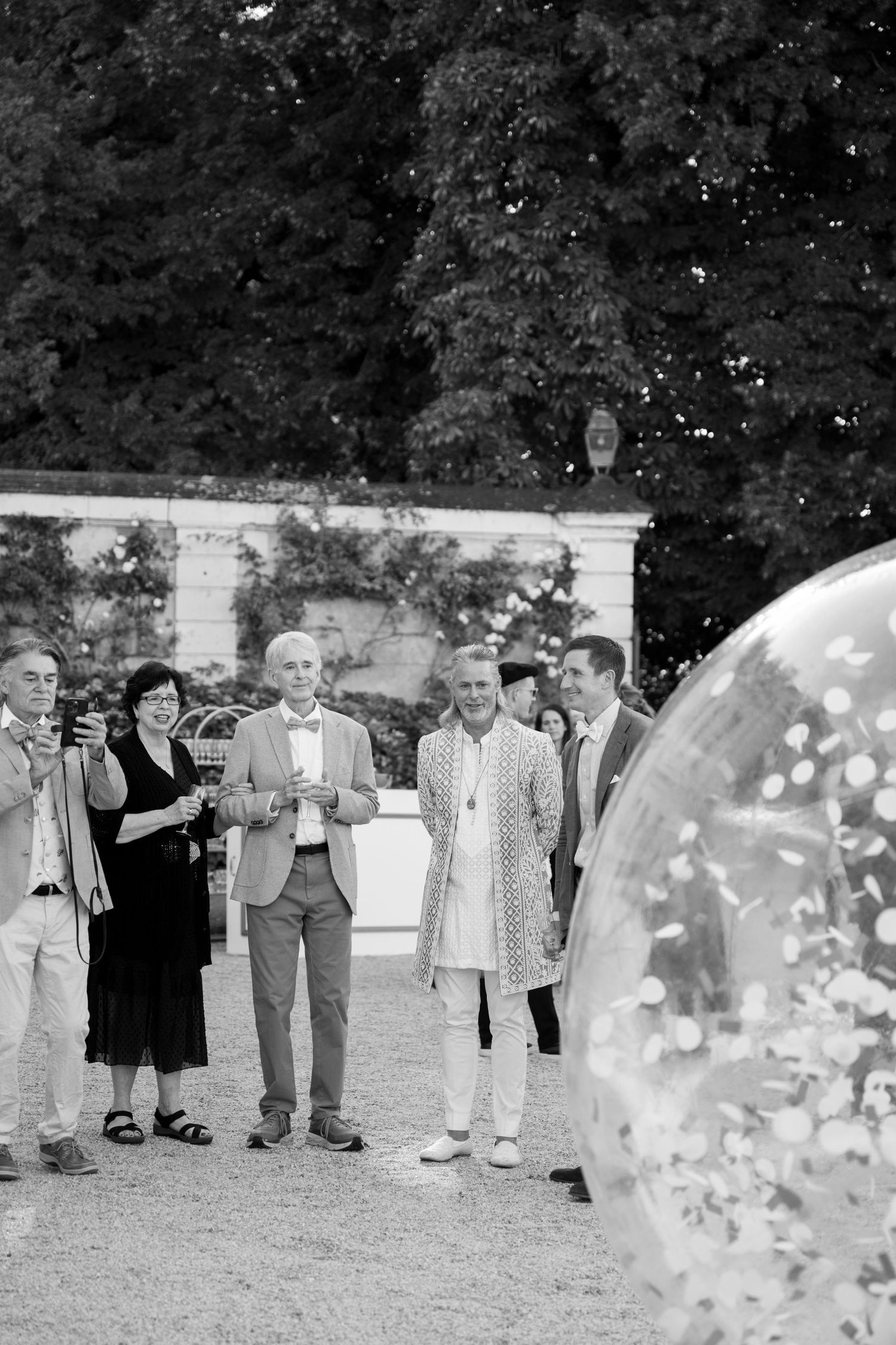 Black and white photo of wedding guests gathered outdoors near large transparent bubble.