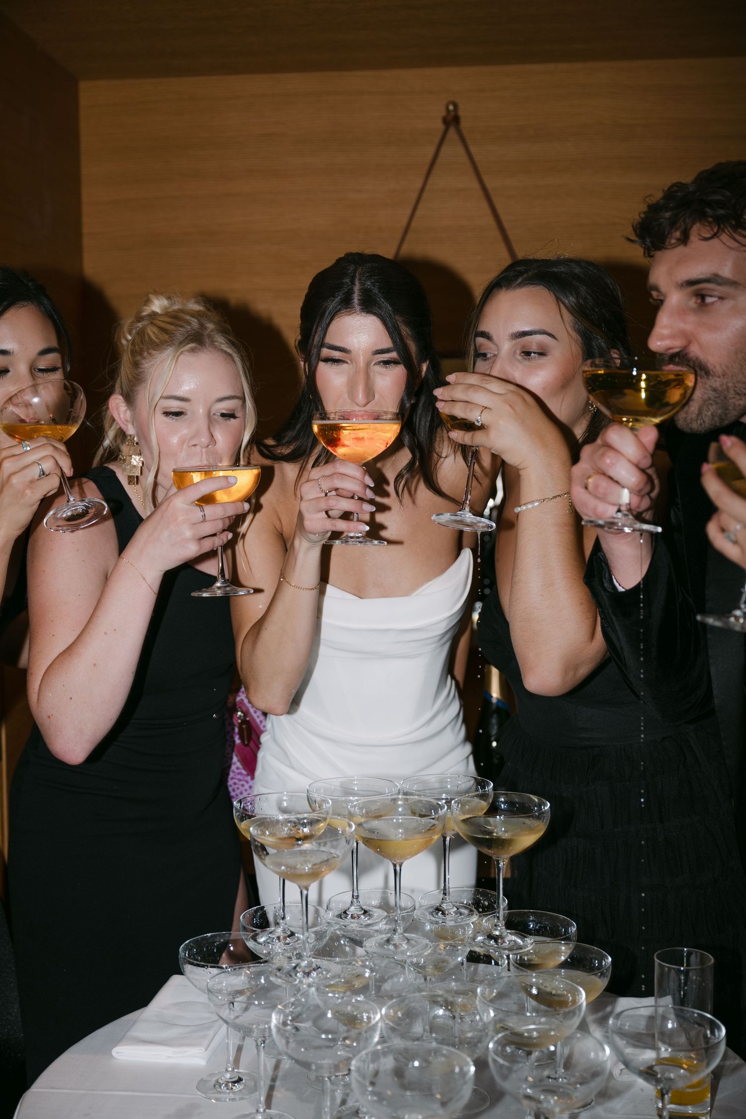 Bride in white gown and guests in black dresses drinking champagne at wedding.
