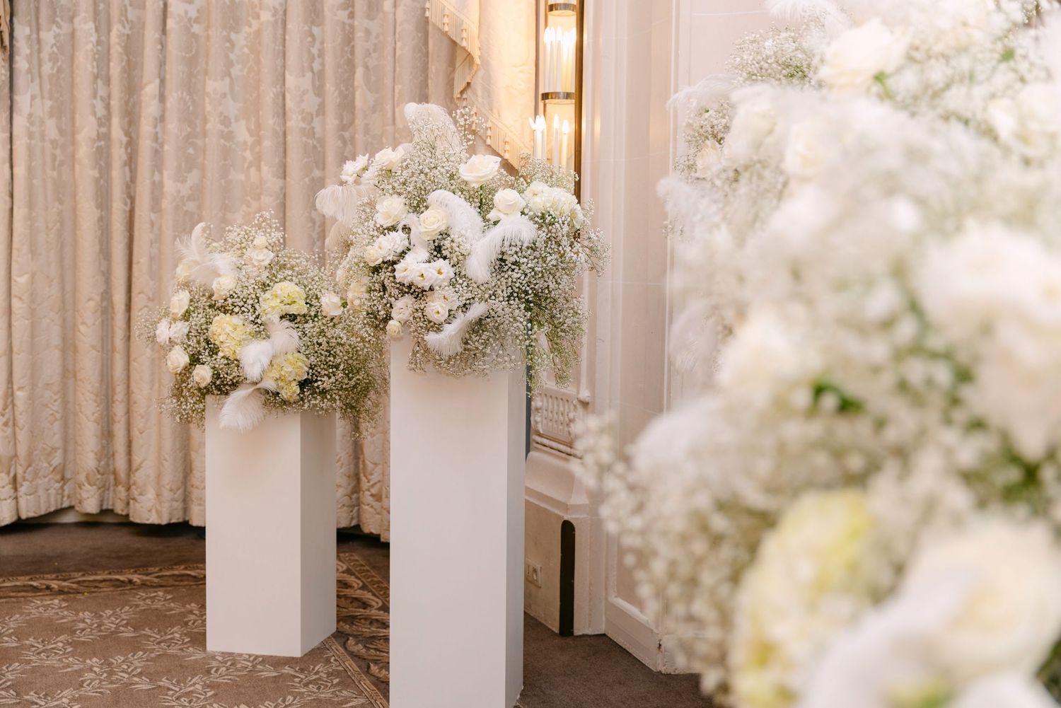 Elegant white floral arrangements on pedestals featuring baby's breath and roses at wedding ceremony altar.