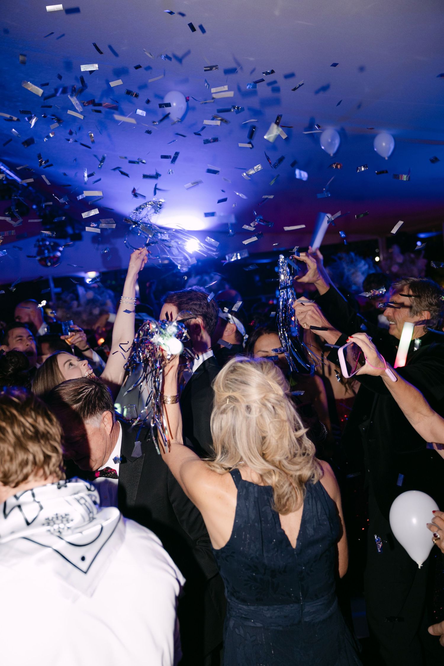 Guests celebrating with confetti and balloons under blue lights at festive evening party.