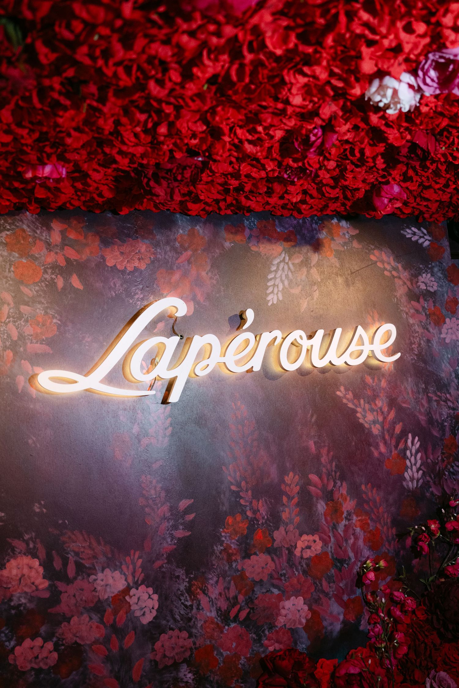 Illuminated Laperouse restaurant sign surrounded by lush red floral wall decoration in Paris.