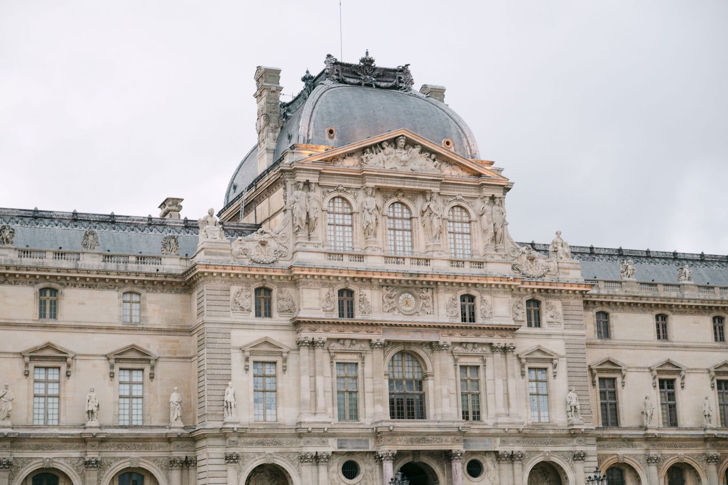 Ornate facade of the Louvre Museum in Paris under a cloudy sky.