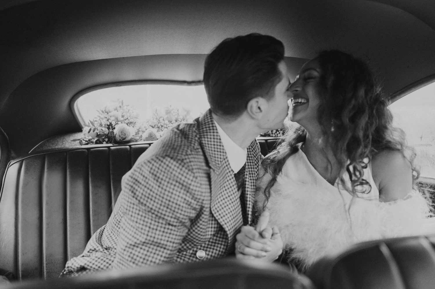 A romantic black and white portrait of a couple sharing an intimate moment in the backseat of a vintage car.