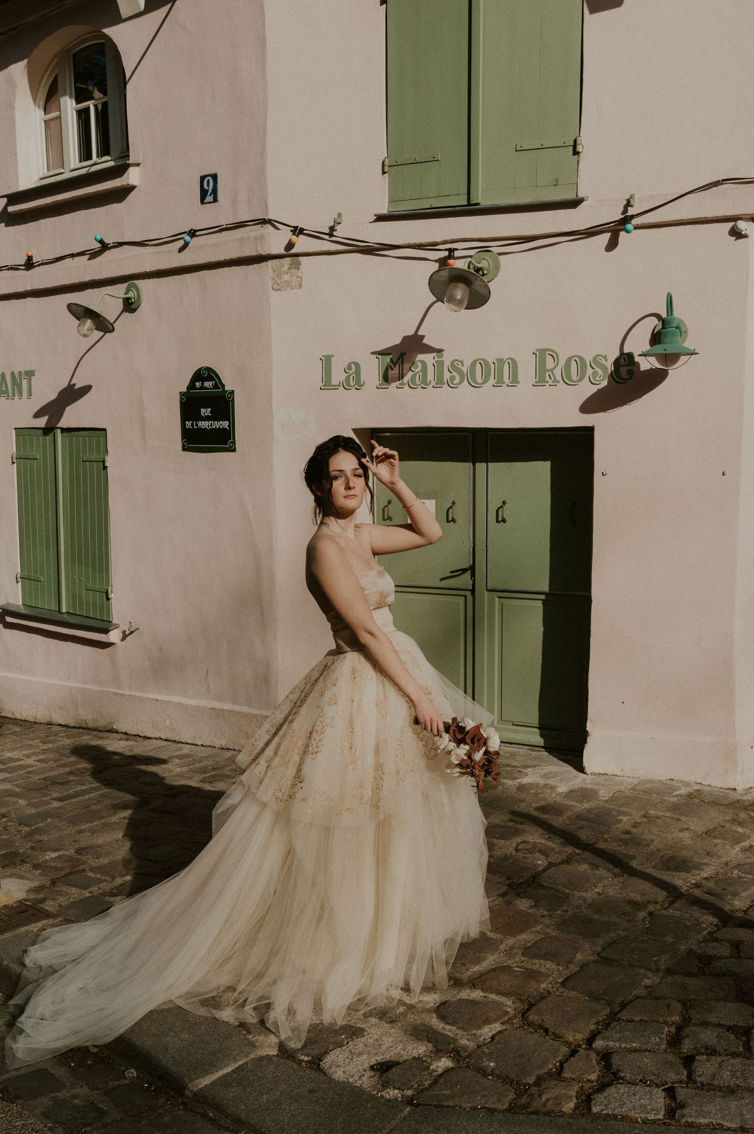 A whimsical bridal portrait in front of La Maison Rose with green shutters and cobblestone streets.