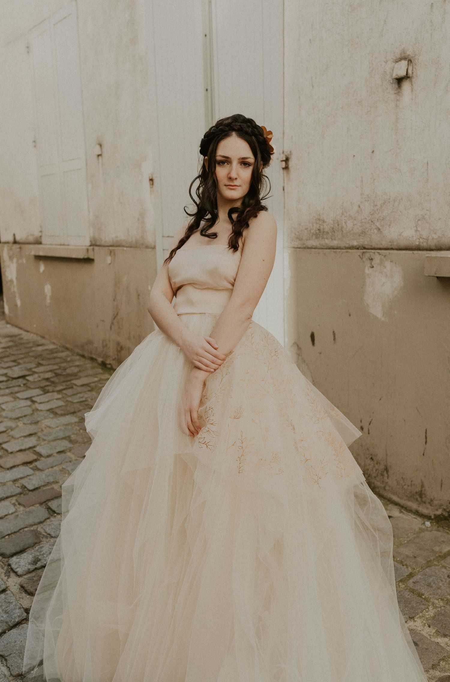 A sepia-toned bridal portrait featuring a strapless ballgown and romantic styling against stone walls.