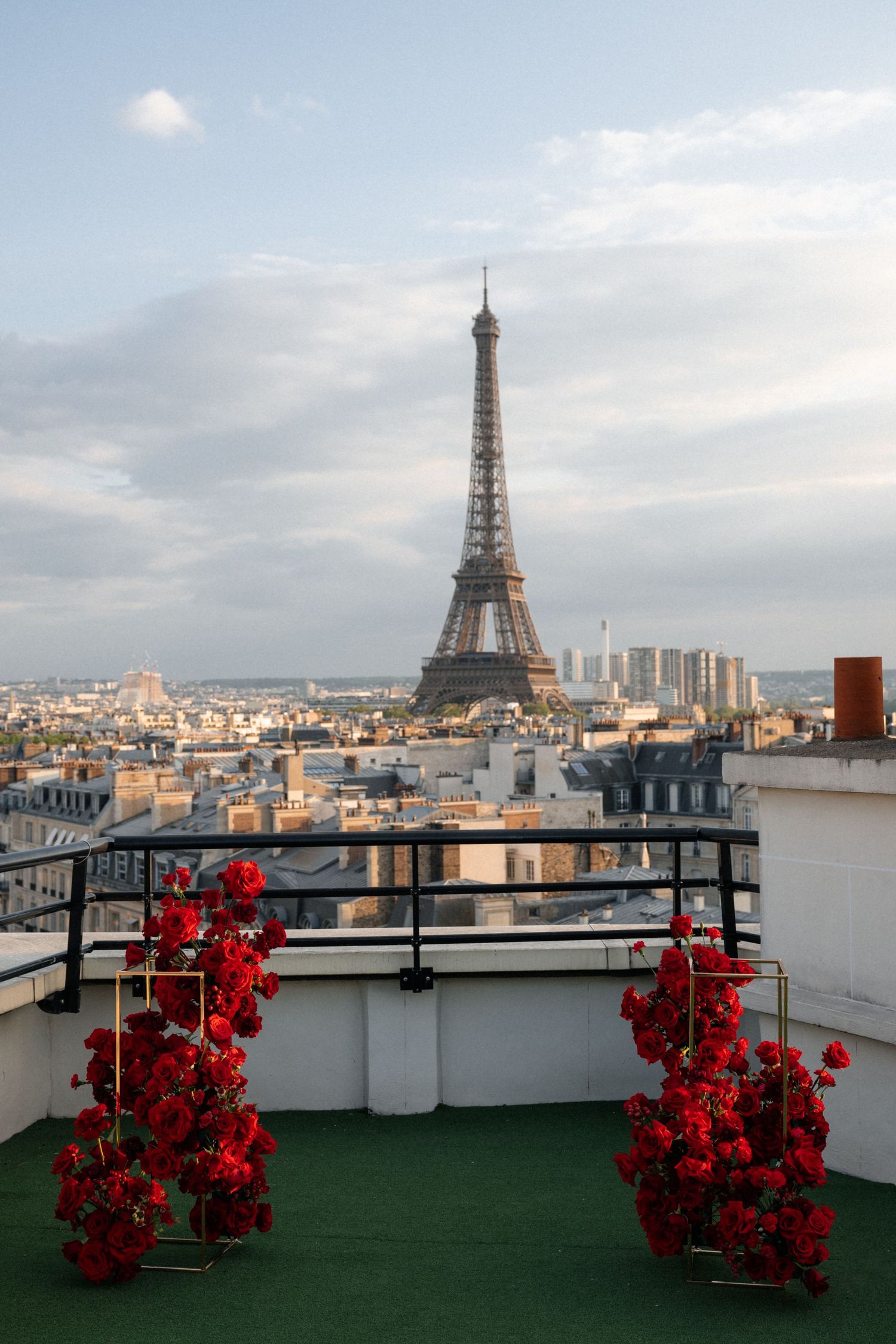Eiffel Tower view from a rooftop terrace decorated with red flowers in Paris, France against a cloudy sky.