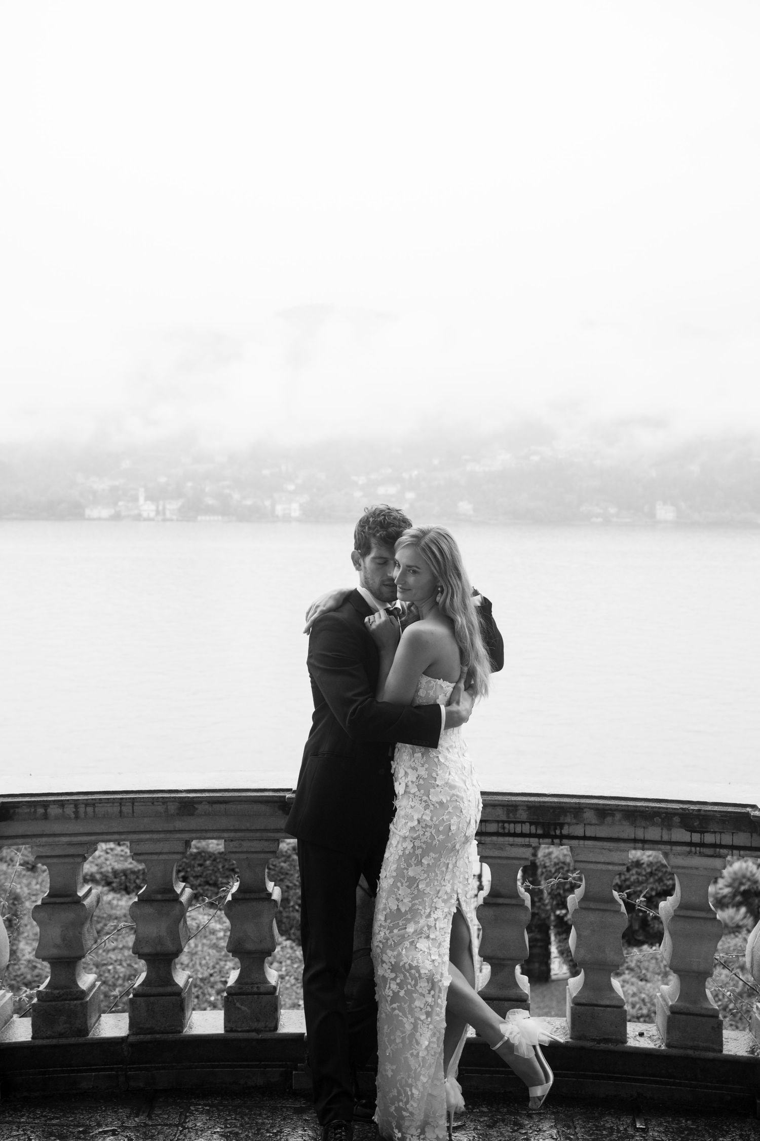 A romantic black and white embrace of a couple at a scenic overlook with cityscape and water views in the background.