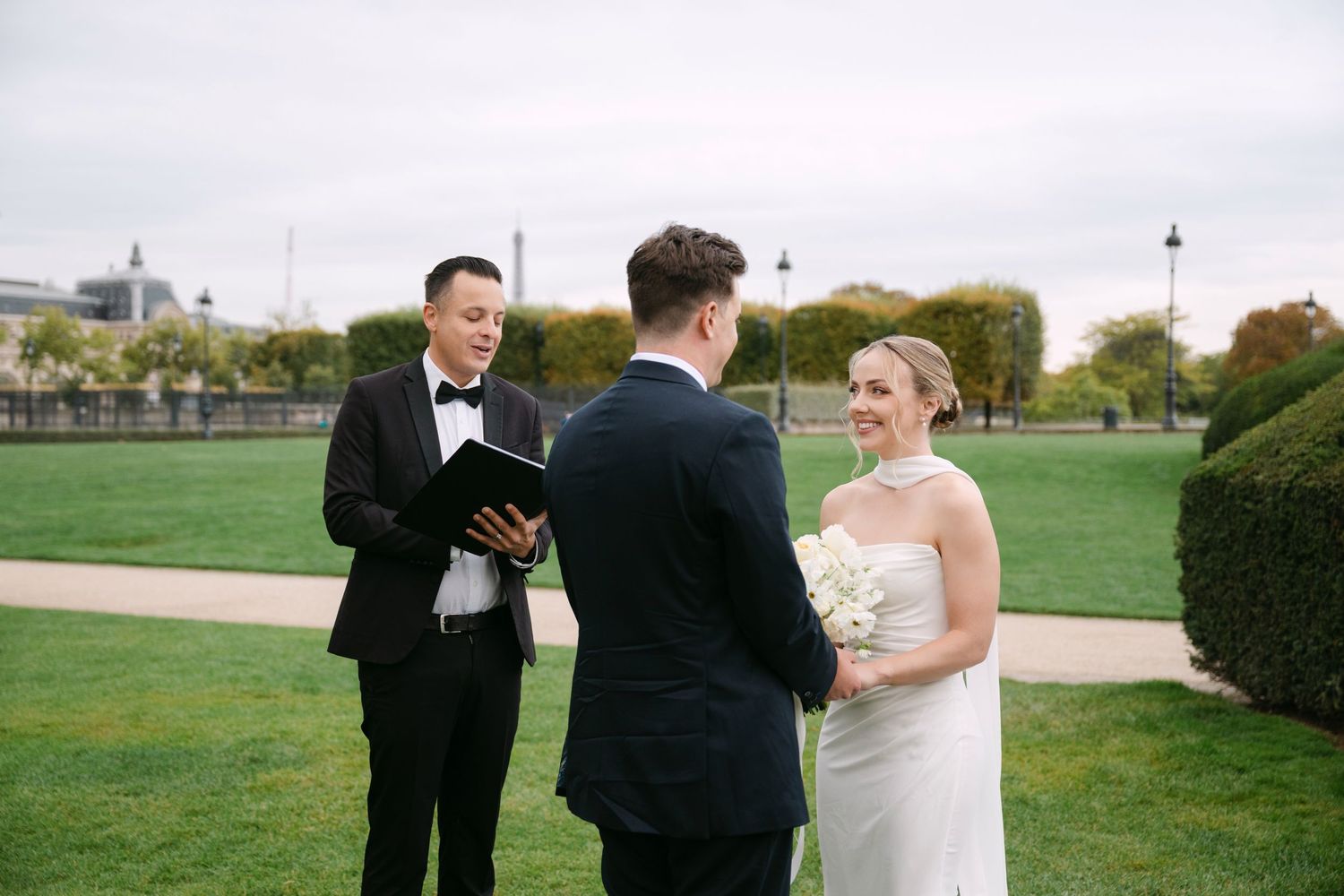 A couple in formal wedding attire shares a joyful moment together outdoors in a garden setting.