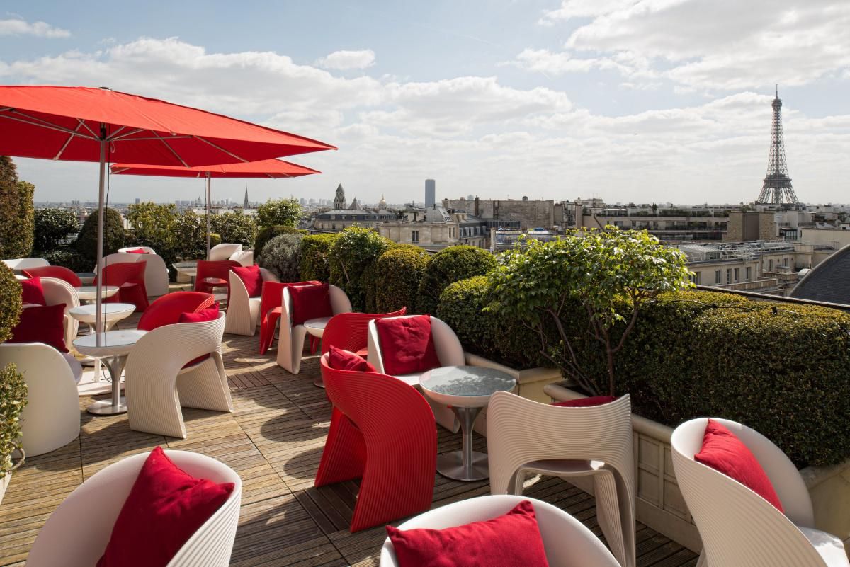Rooftop terrace in Paris with red umbrellas and chairs offering views of the Eiffel Tower.