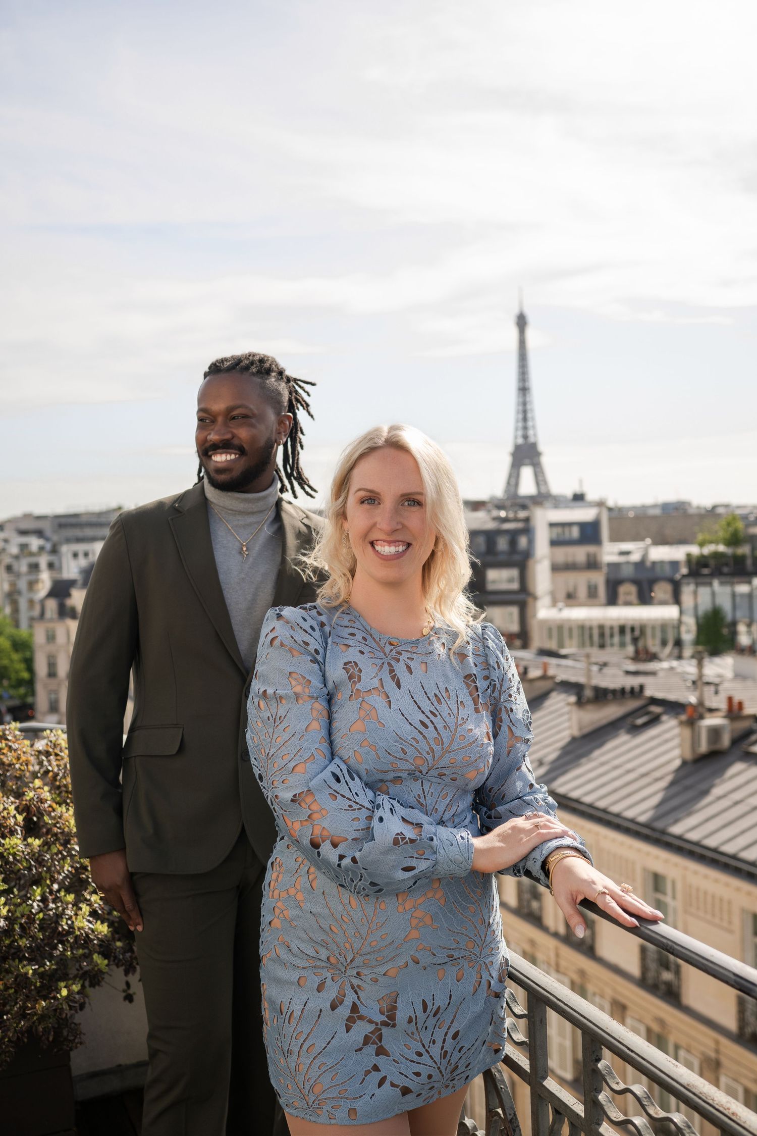 Couple posing on a Paris rooftop terrace with the Eiffel Tower in the background on a sunny day.