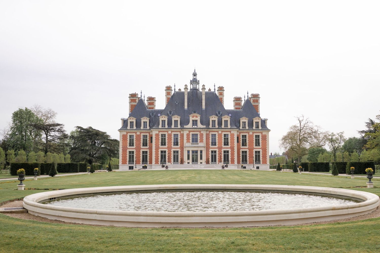 Elegant French château de Nainvilles Roches with symmetrical brick facade, ornate roofline, and circular fountain pond s