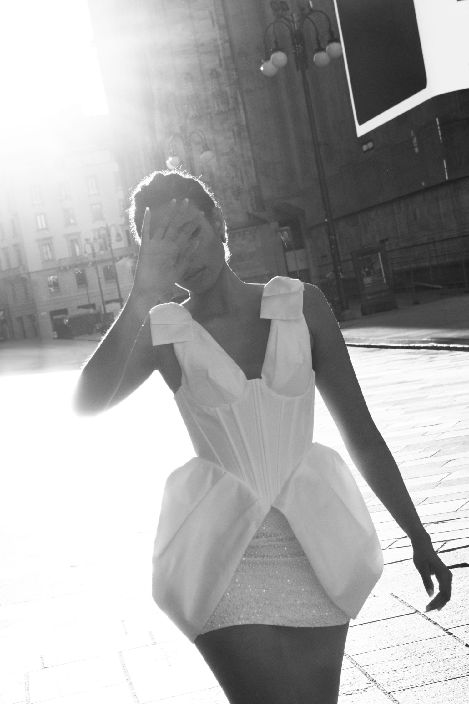 Black and white photo of a bride in a short white dress shielding her eyes from bright sunlight.