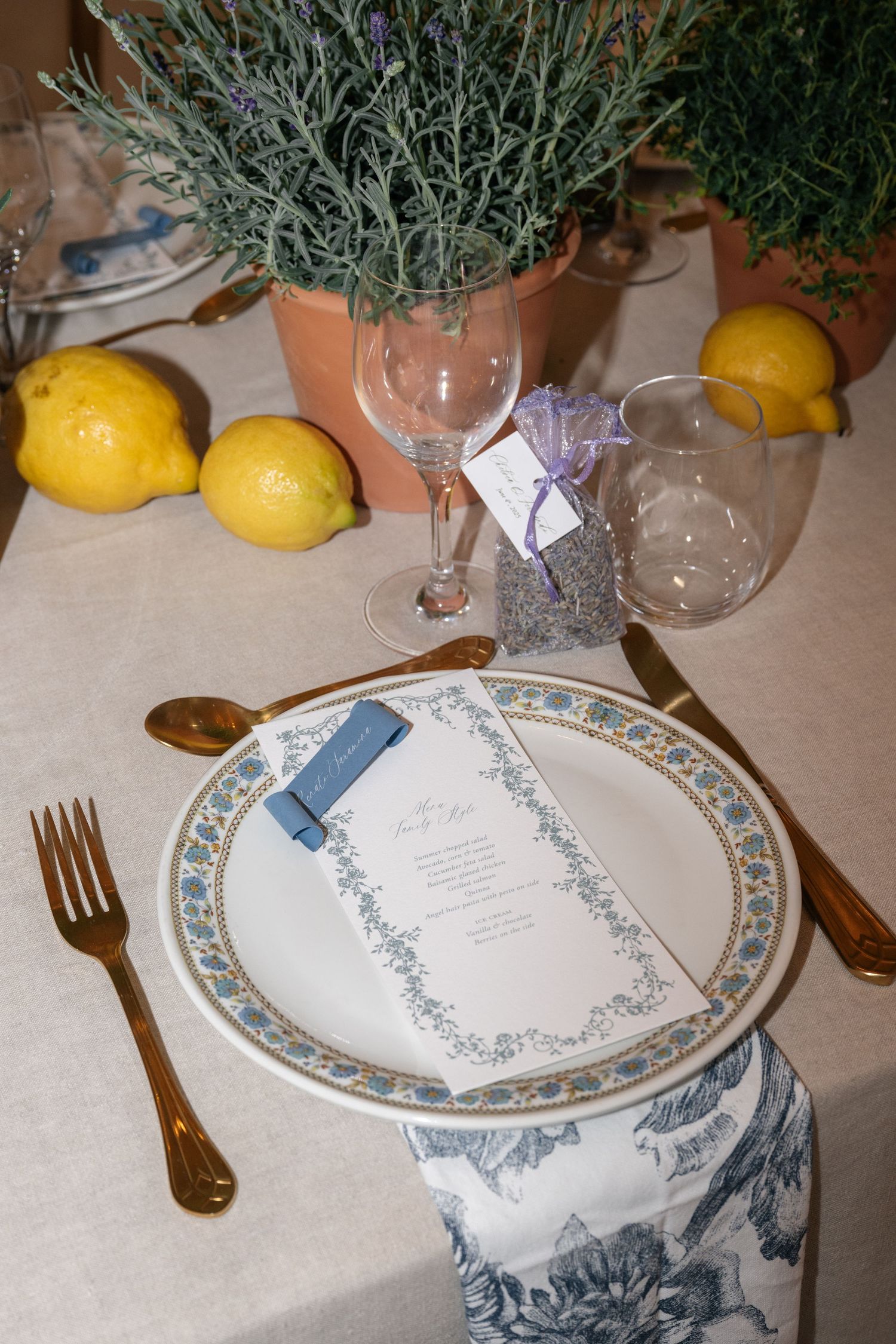 Place settings with decorative plates, lemons, and lavender sprigs on a cream-colored tablecloth create an elegant dining scene.