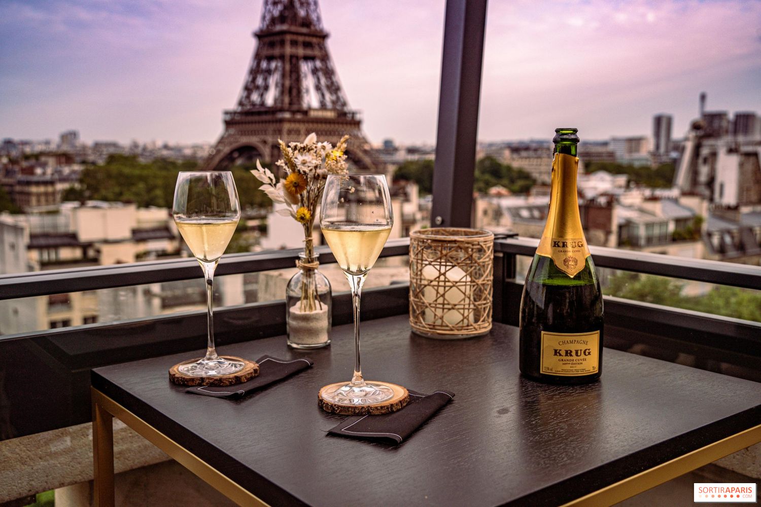 Champagne glasses and bottle on a balcony table with the Eiffel Tower lit up in the background.