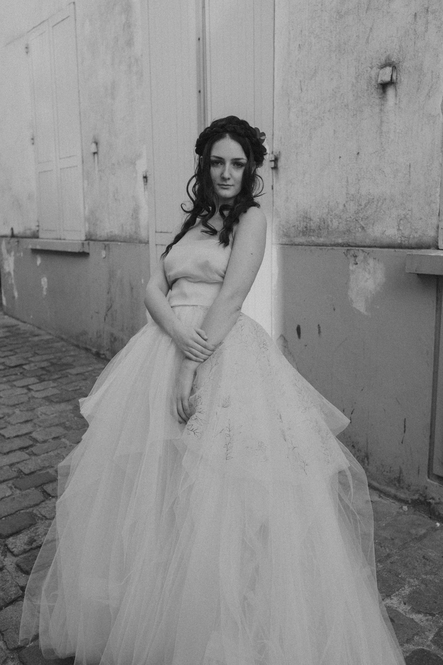 A black and white portrait of a bride in a strapless ballgown against weathered stone walls.