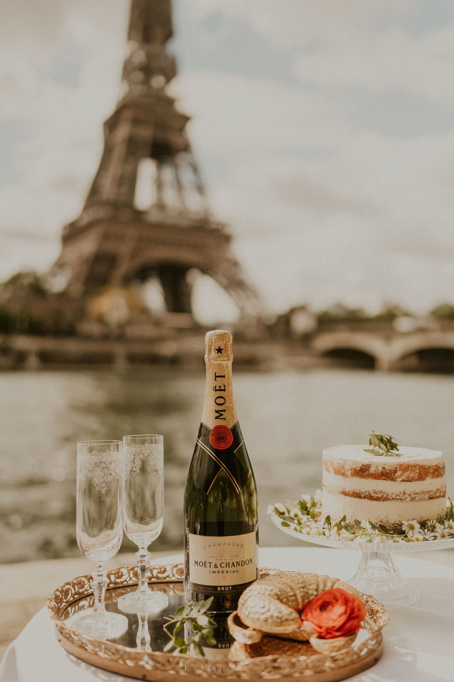 Champagne bottle and glasses set against the Eiffel Tower backdrop with elegant desserts.