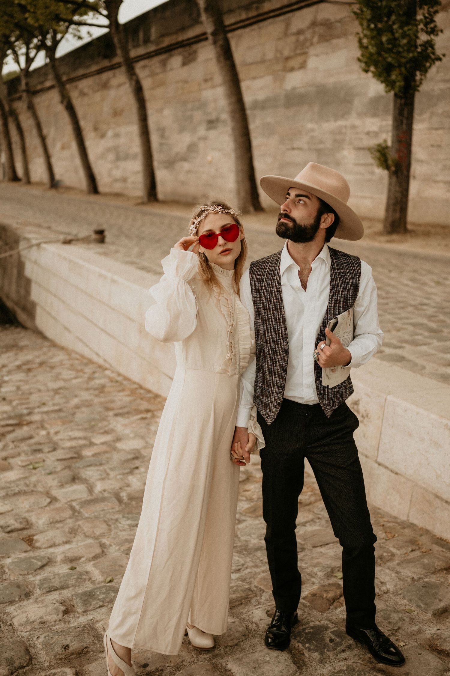 A retro-inspired couple pose against stone architecture wearing red sunglasses and vintage attire.